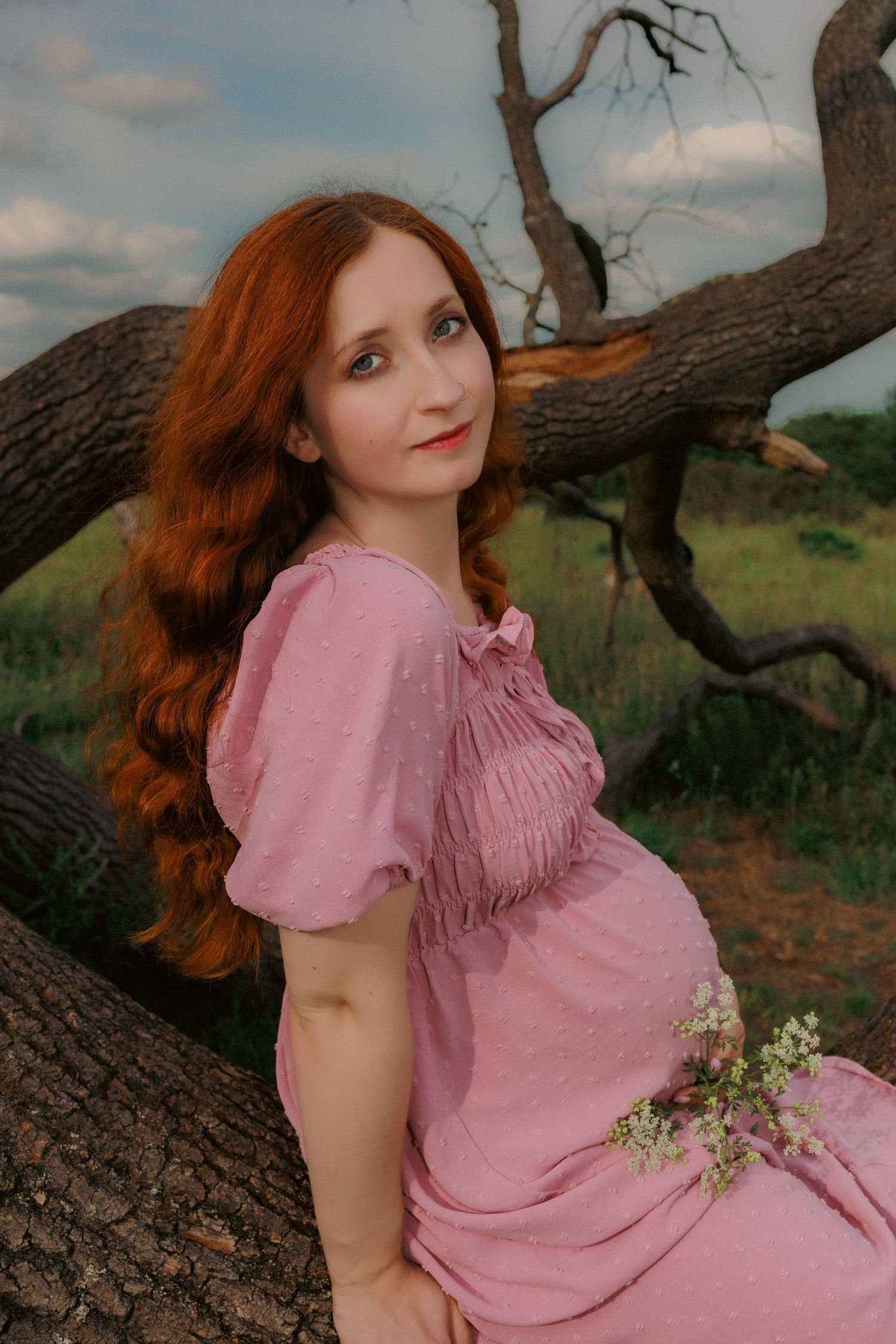 Portrait of redhead pregnant women in pink,sitting on tree, during her empowerment maternity photoshoot in nature capture by Untamed muses