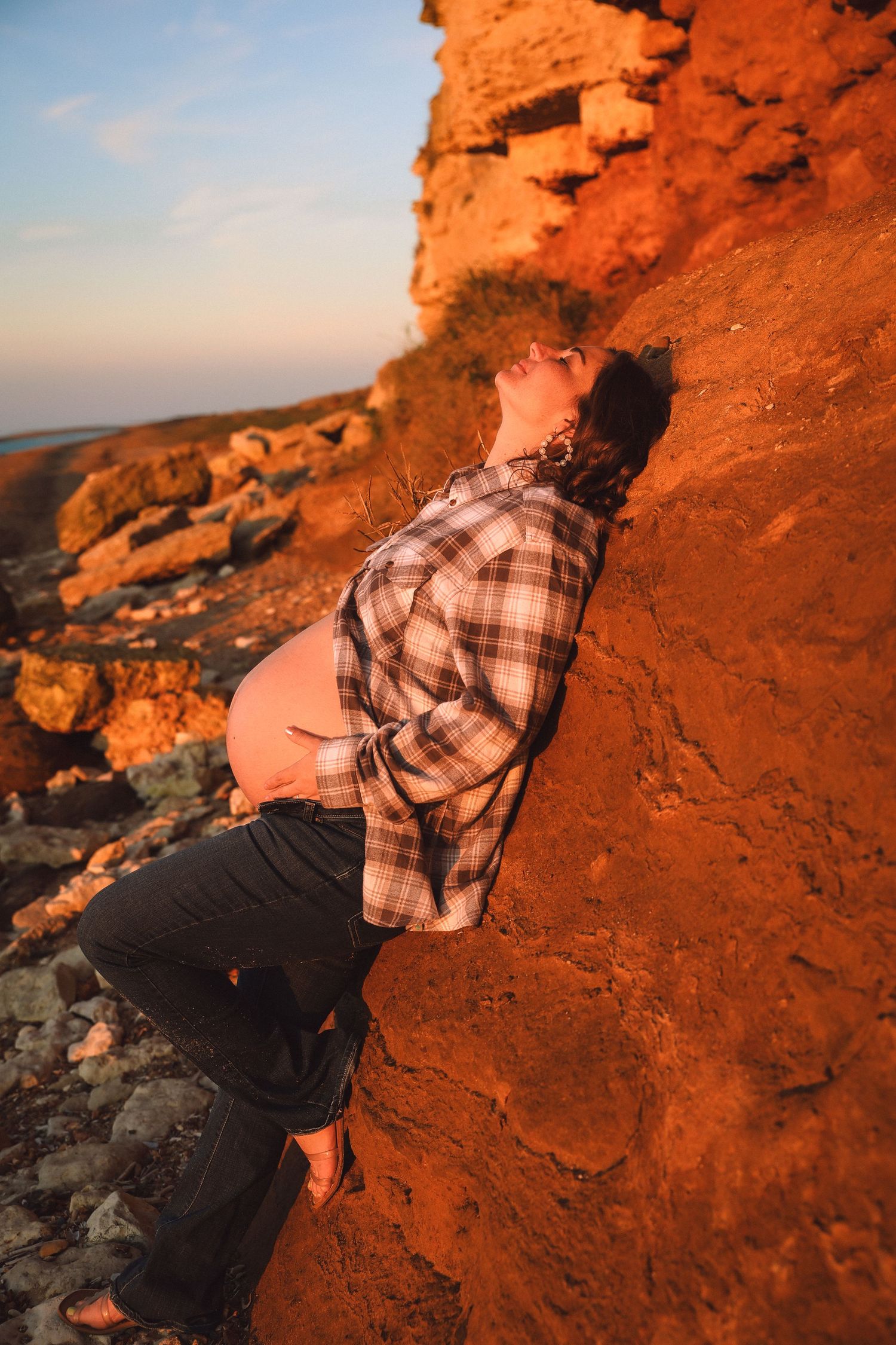 Sunset at the coast  pregnant woman leaning agains a cliff wall, empowerment, maternity by  published female gaze photographerUntamed Muses