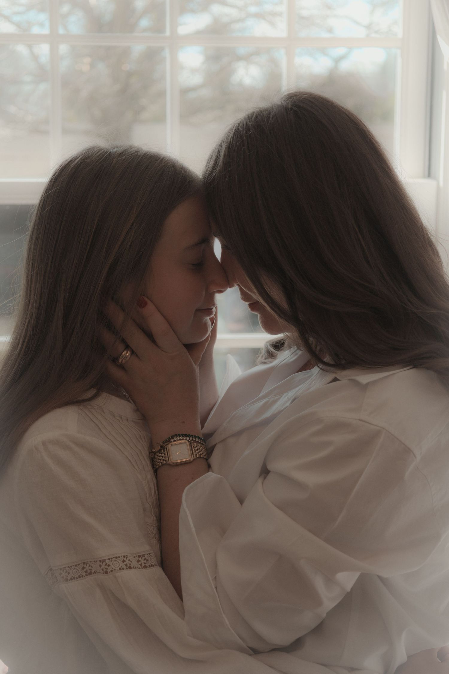 close up portrait on mum holding daughters face to hers ,in front of window, soft natural light, grainy