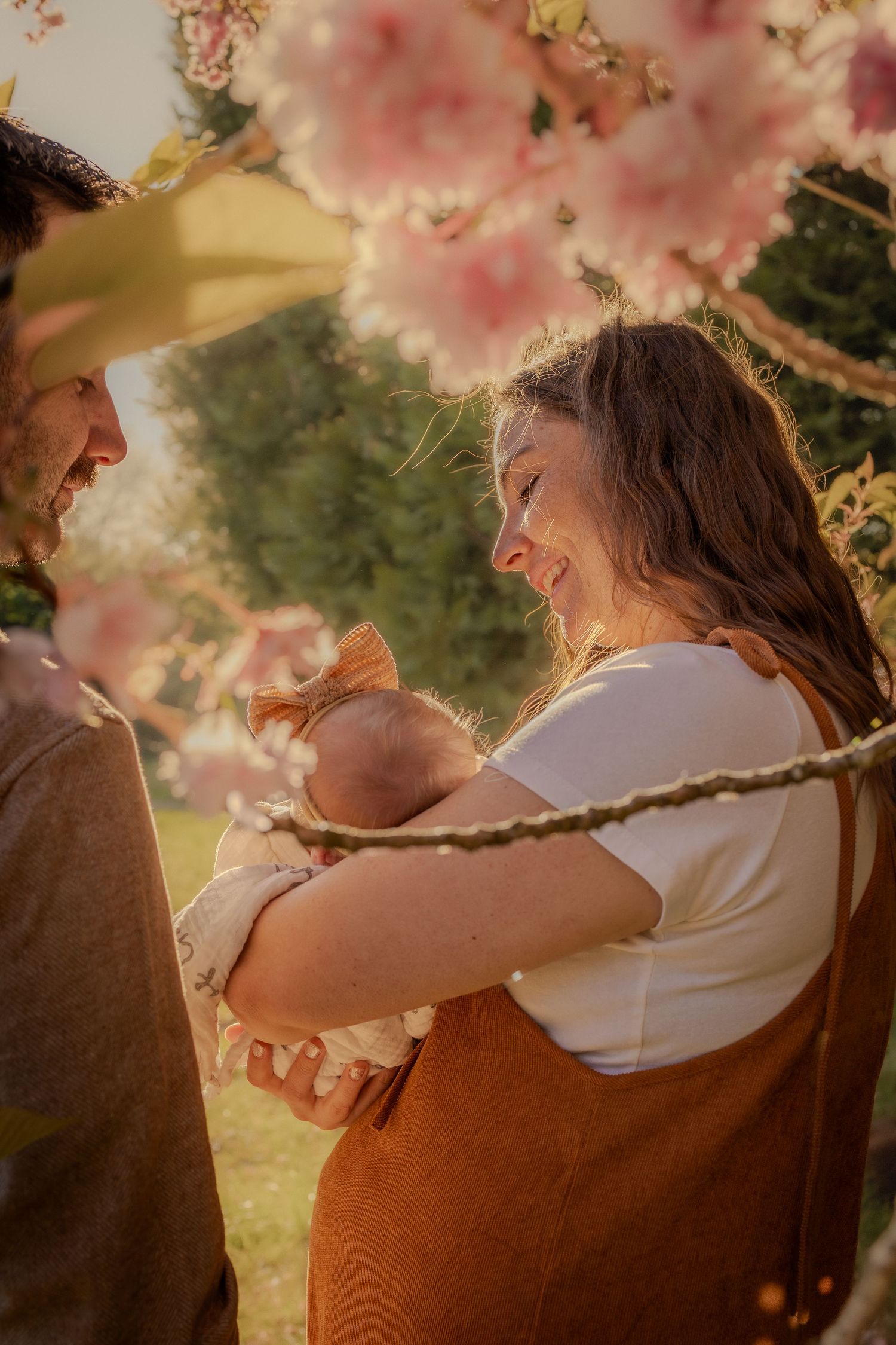 capture of family with newborn framed by blossoms and branches , natural newborn photoshoot in nature by untamed muses in thetford