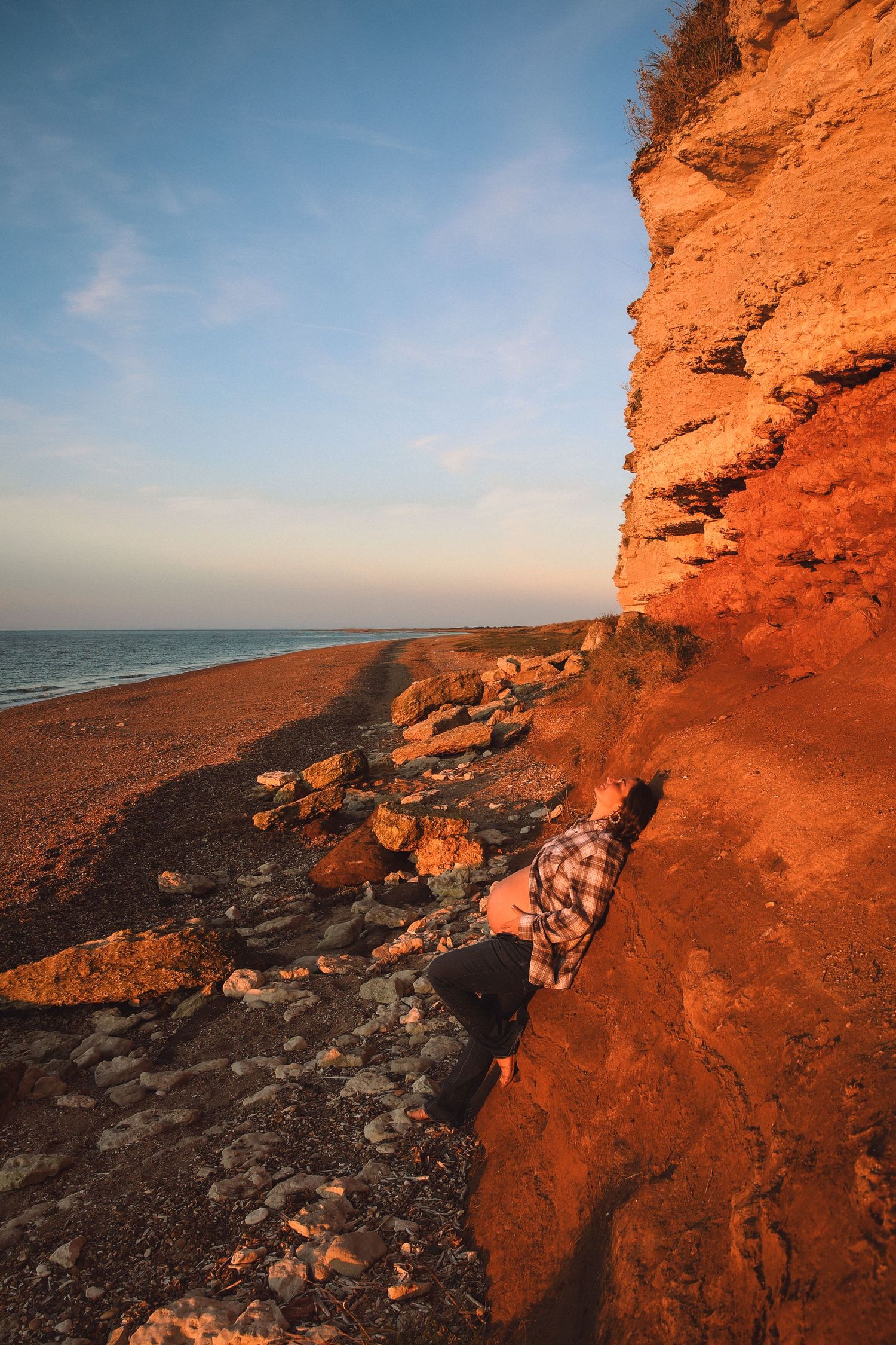 Sunset at the coast  pregnant woman leaning agains a cliff wall, empowerment, maternity by  published female gaze photographerUntamed Muses