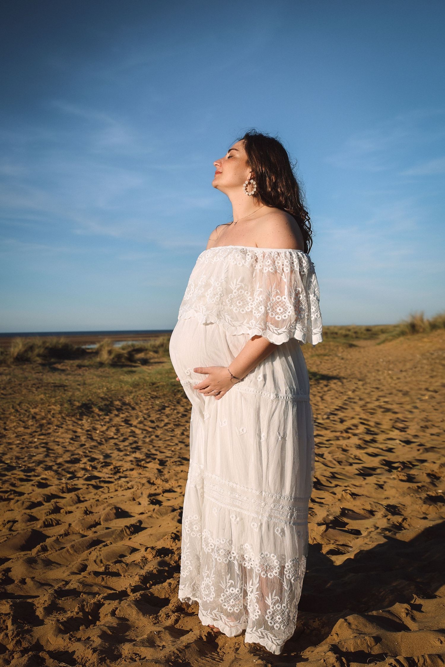 Powerful portrait of pregnant women in the Norfolk coast, holding bump, eyes closed, wind gentle swapping her hair, Maternity outdoors