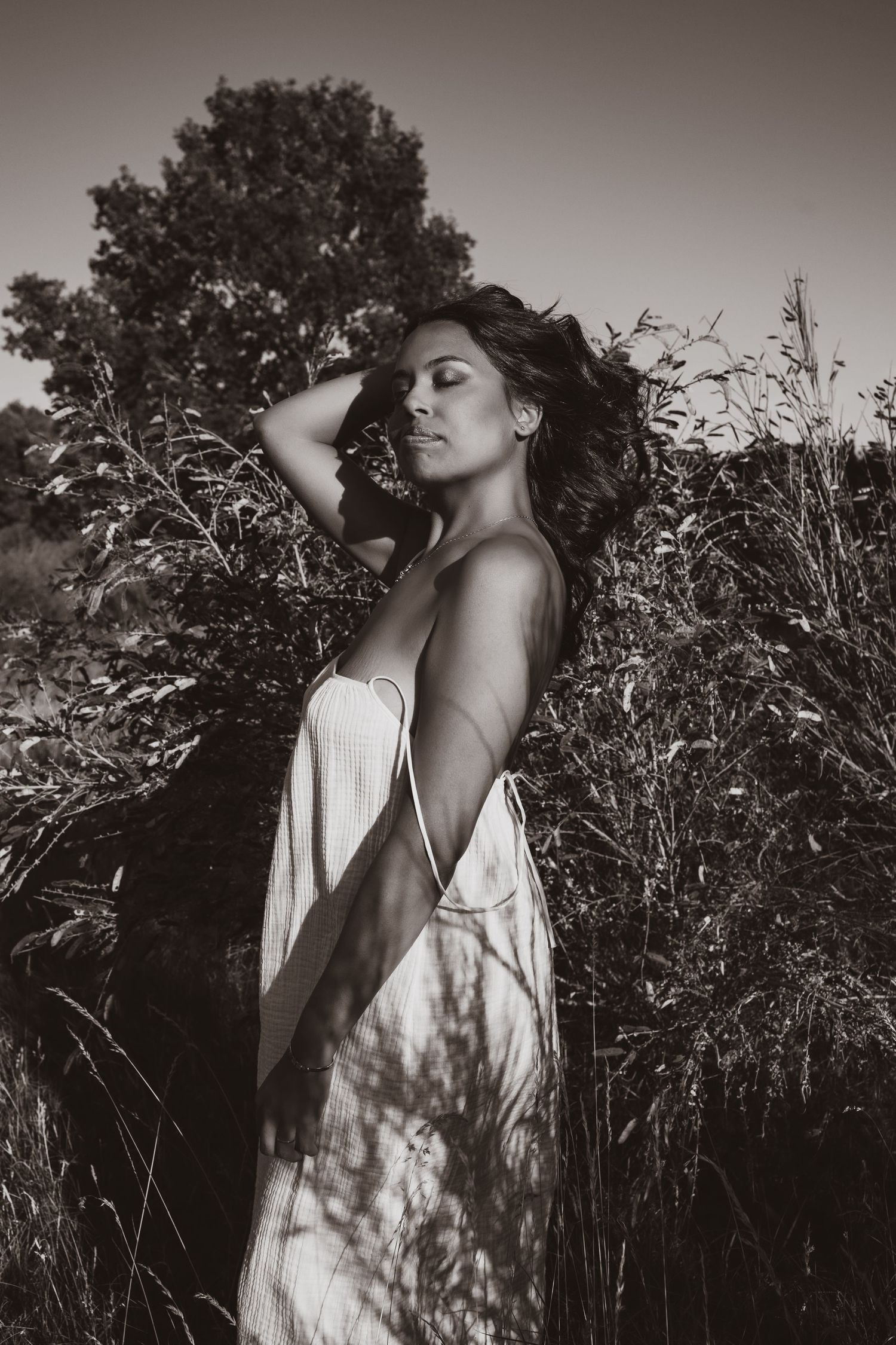 Empowerment photography in Norfolk. Woman amidst tall grass, hair blowing with the wind, female gaze photographer. Monochrome
