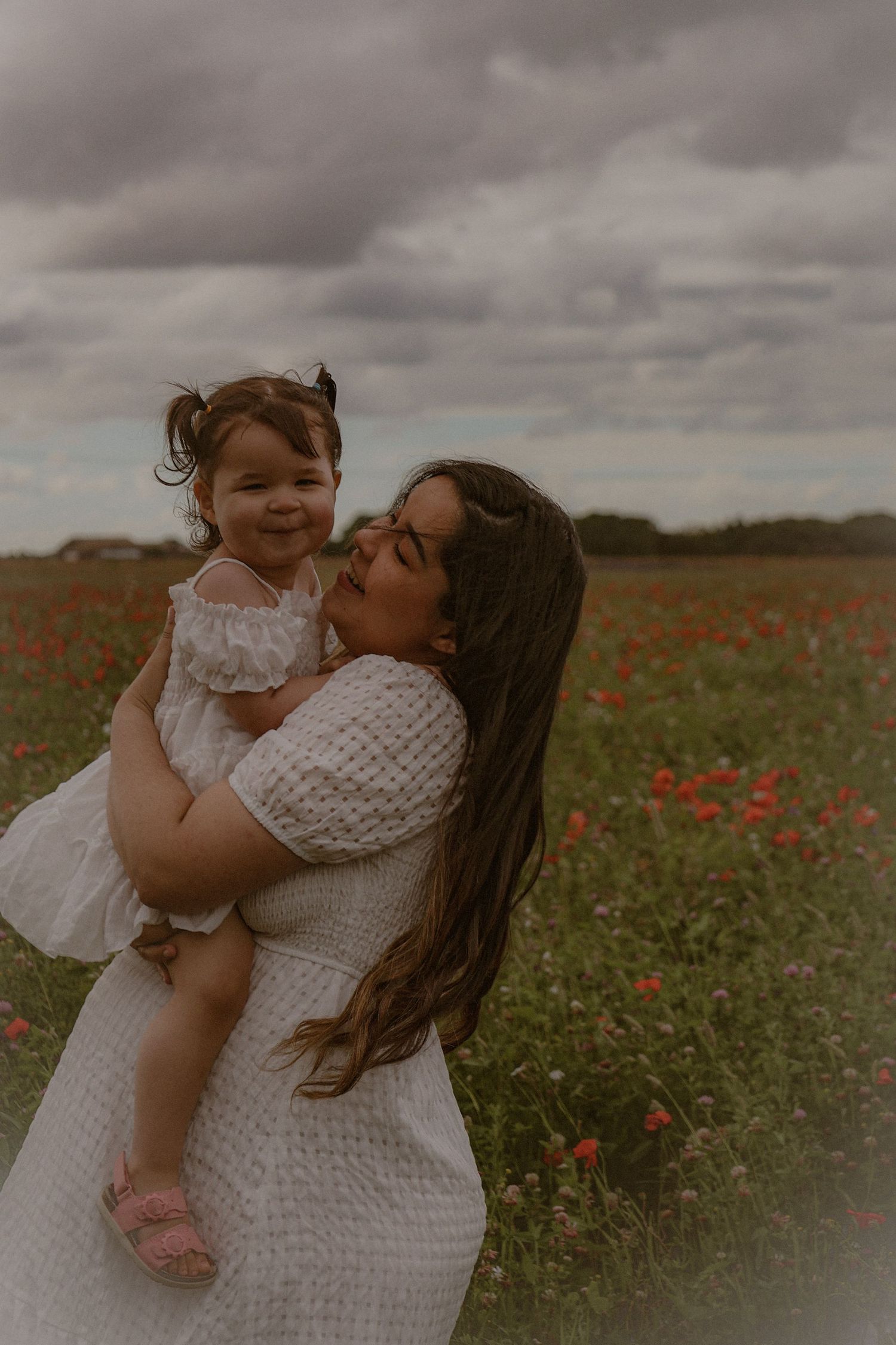 cinematic,  portrait of woman and her little girl  in a wild flower field in Suffolk, captured by Untamed Muses, moody skies