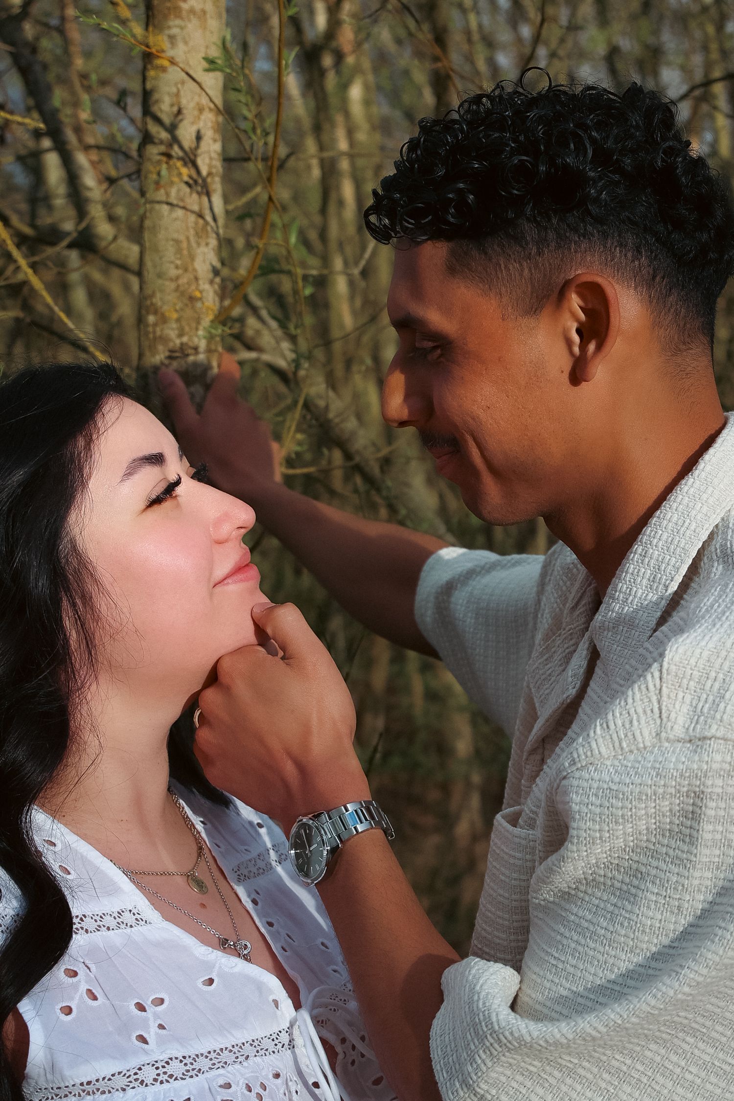 Couple staring into each others eyes leaning on a tree, him lifting her chin up lovingly, passionate, emotive photography by untamed muses