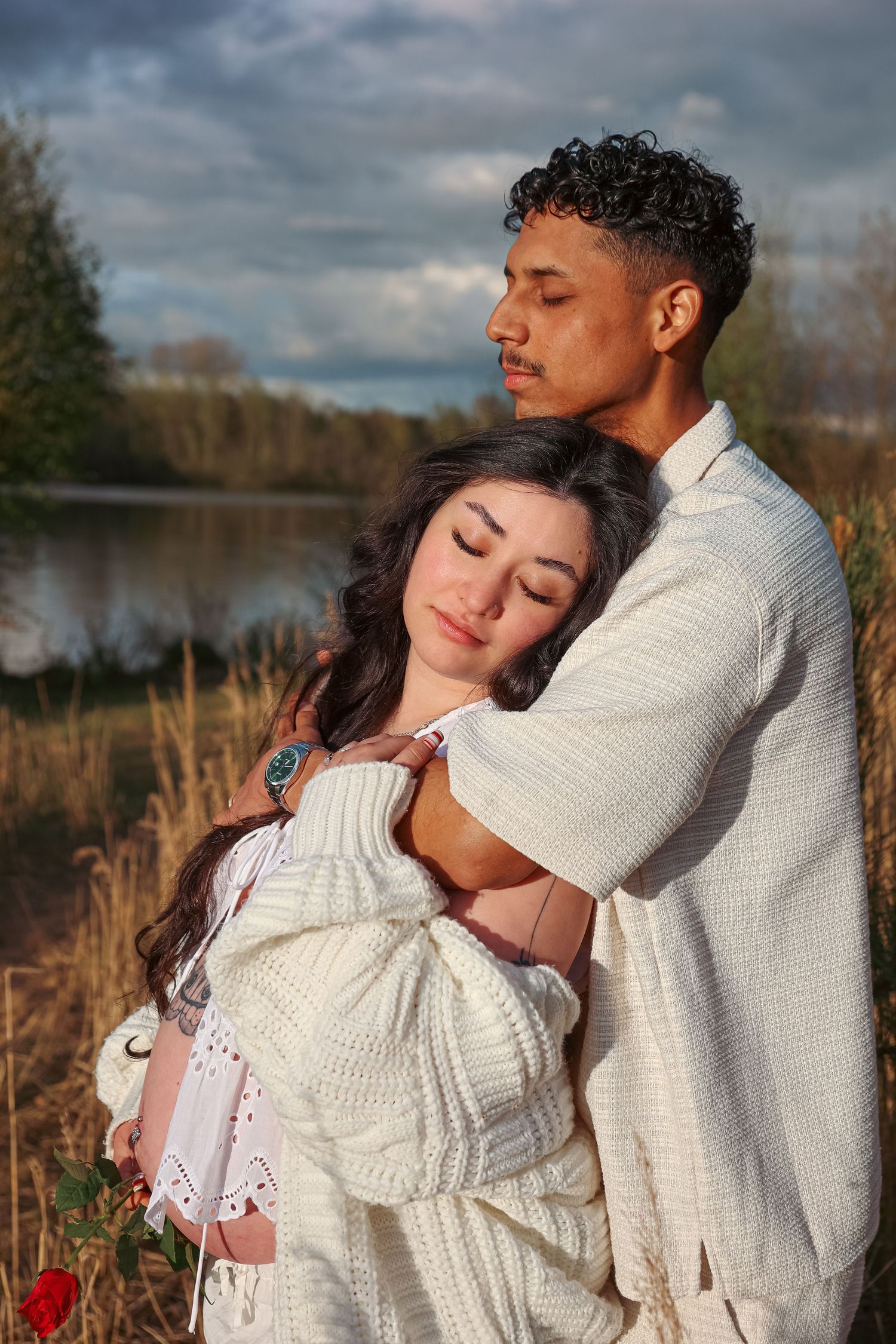 Man holding wife adoringly from behind, peaceful beautiful moment during maternity photoshoot by a lake in Norfolk by Untamed Muses
