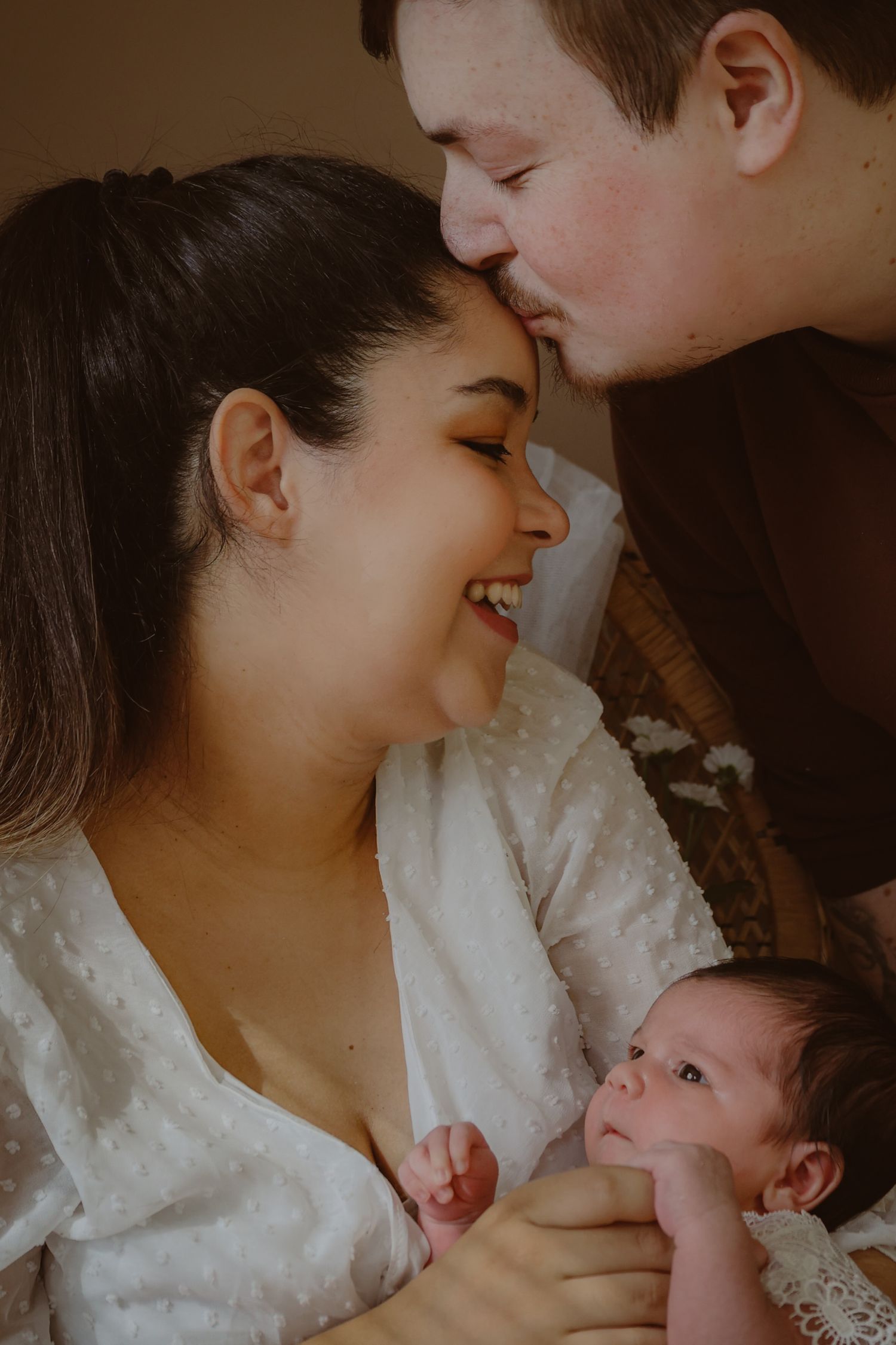 At home natural newborn family, dad kissing mum on forehead while she smiles holding their baby girl, thetford newborn lifestyle photography