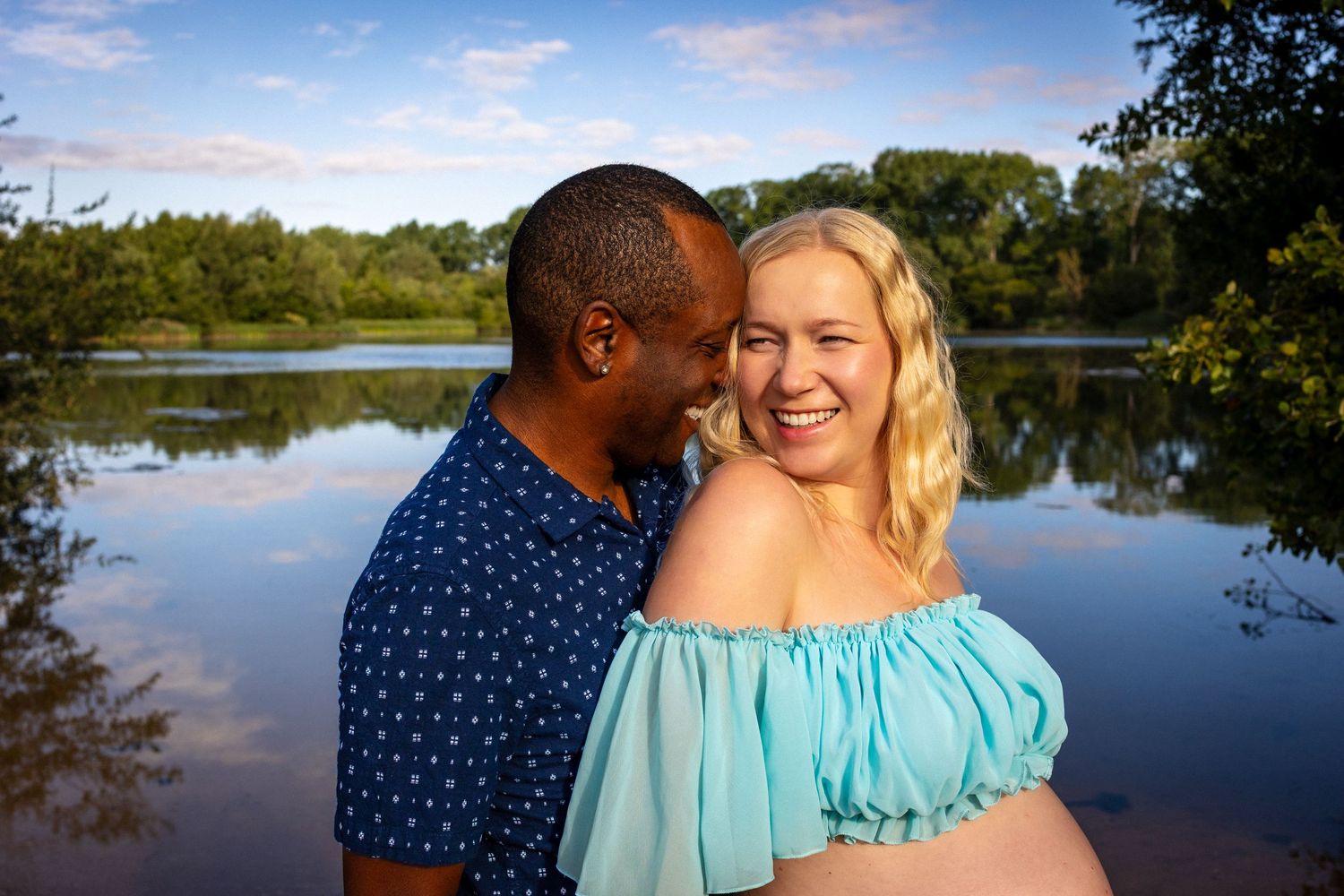 Portrait of soon to be interracial parents, joyful, holding each other by a stunning lake captured by Untamed Muses
