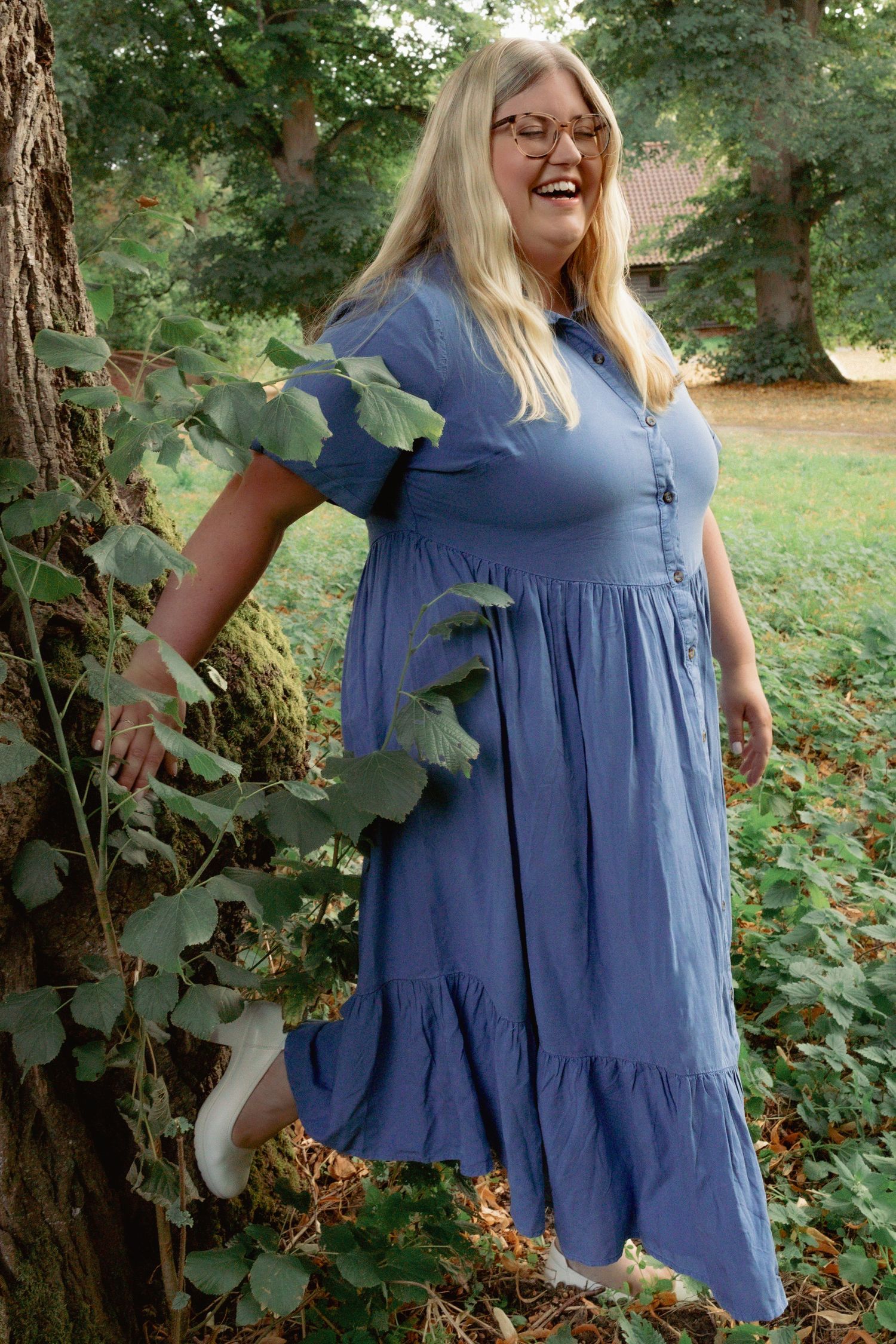 Persona branding portrait of woman in blue dress half leaning on a tree, laughing, natural beauty and natural light