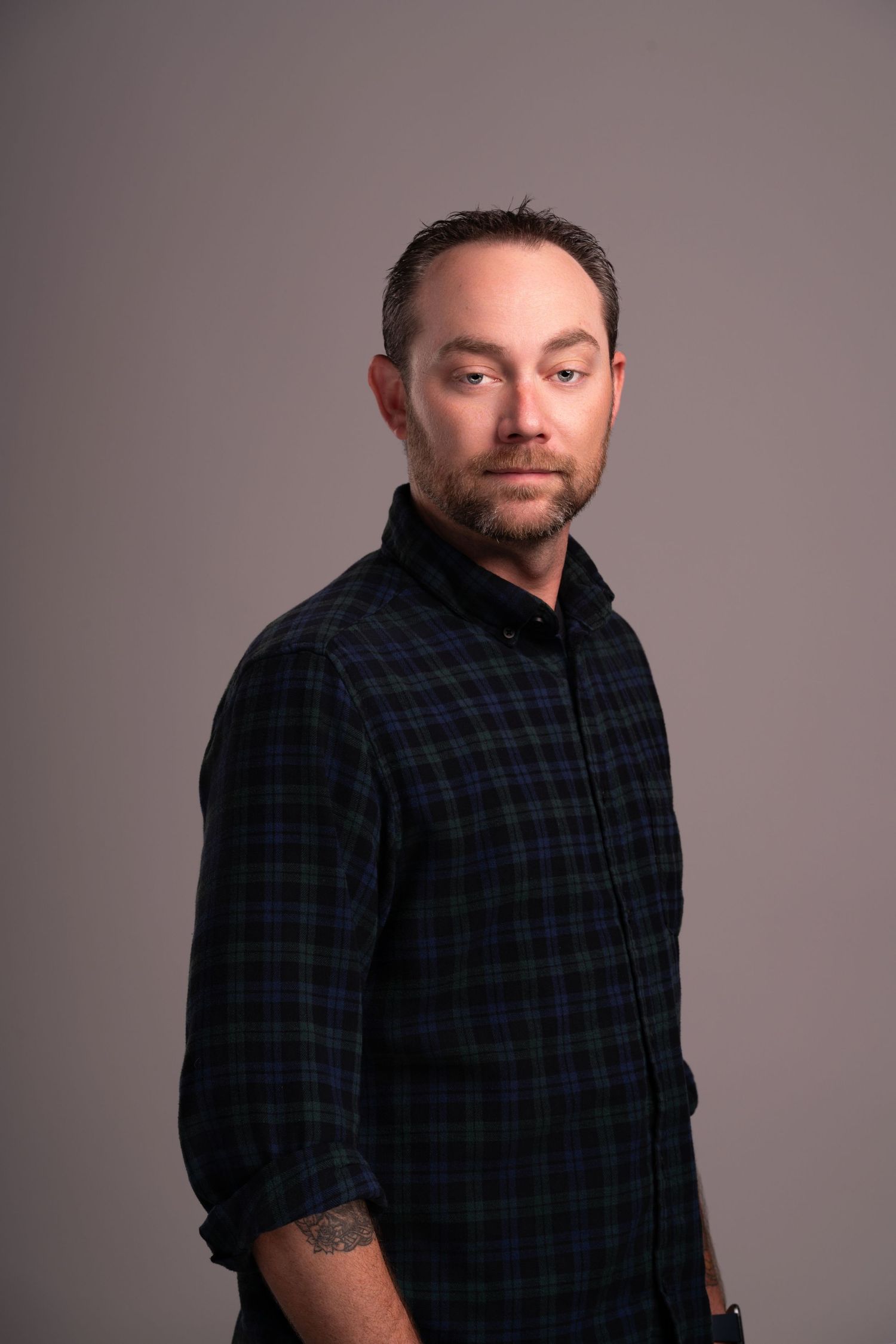 Portrait of person in plaid flannel shirt against neutral background.