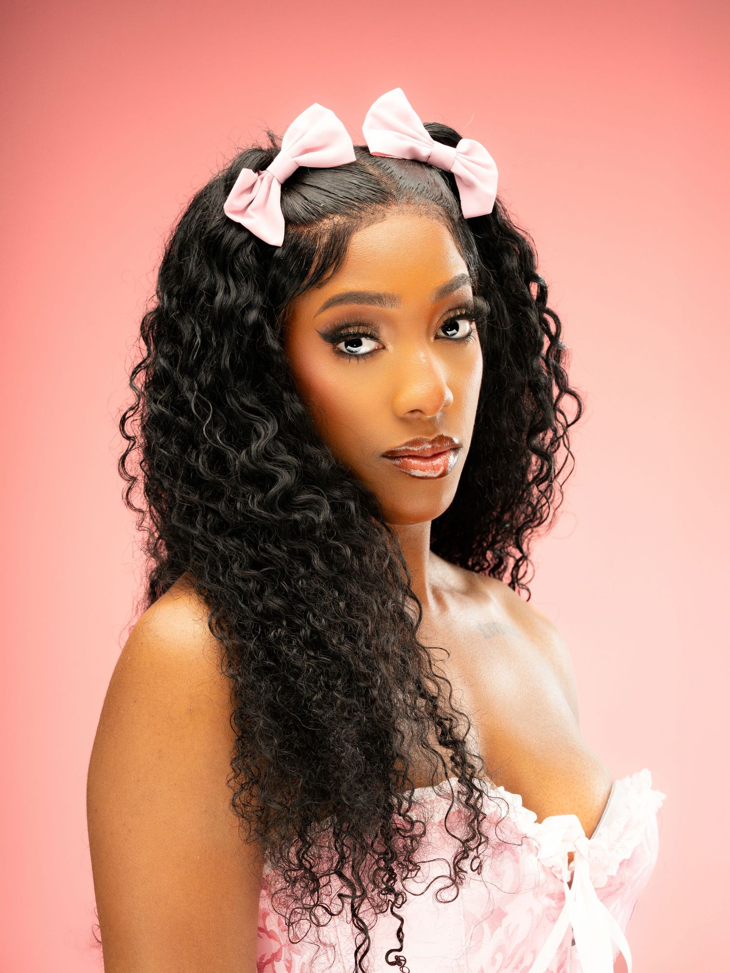 Studio portrait with curly hair adorned with white bows against a pink backdrop.