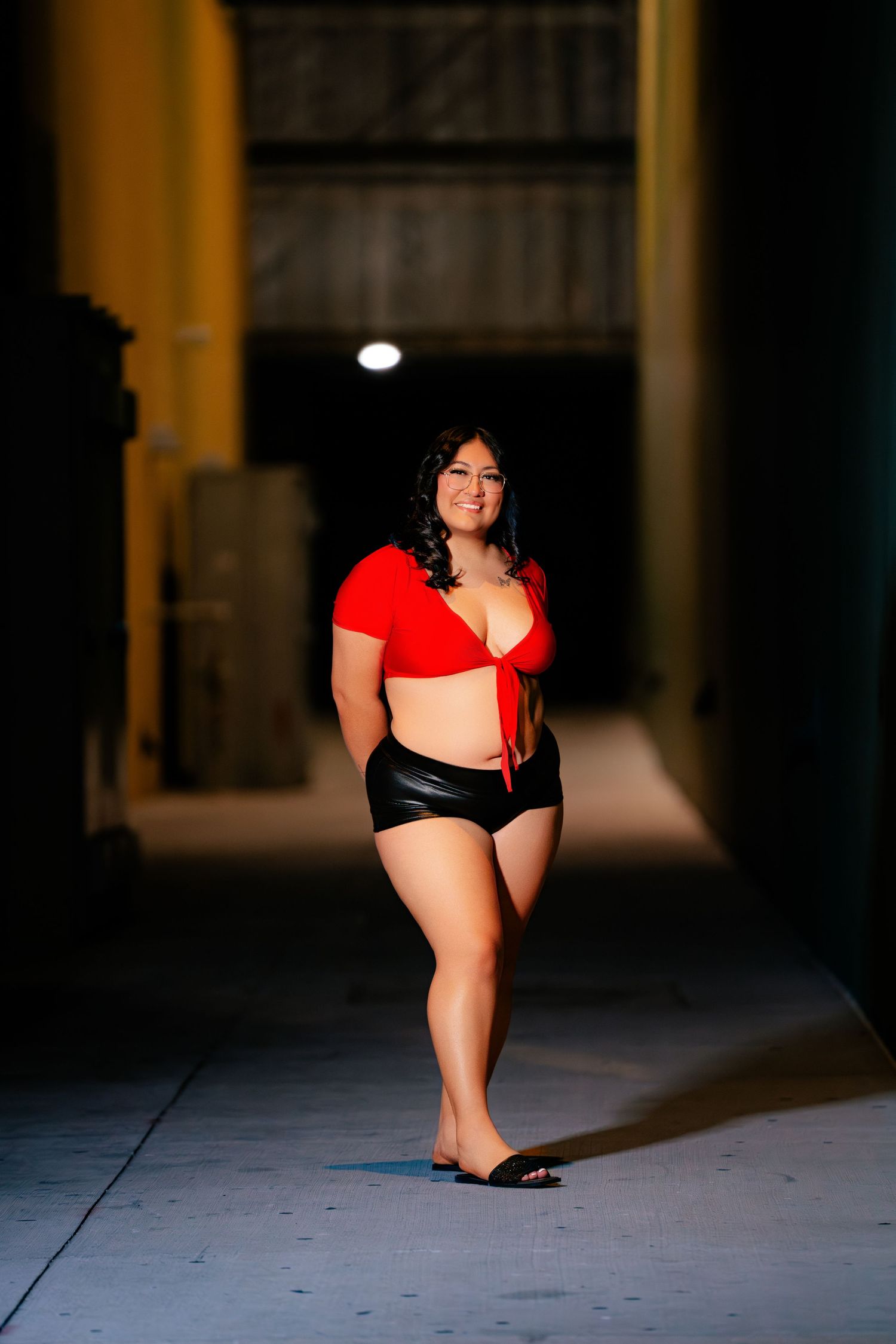A person in red athletic wear poses dramatically in a dimly lit corridor with concrete pillars.