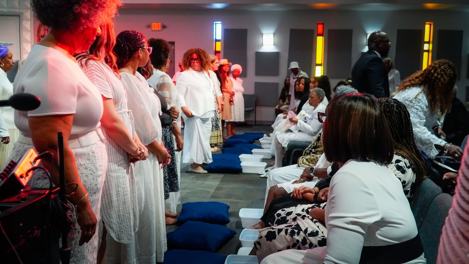 Church members dressed in white stand in formation during a special service with red ambient lighting.