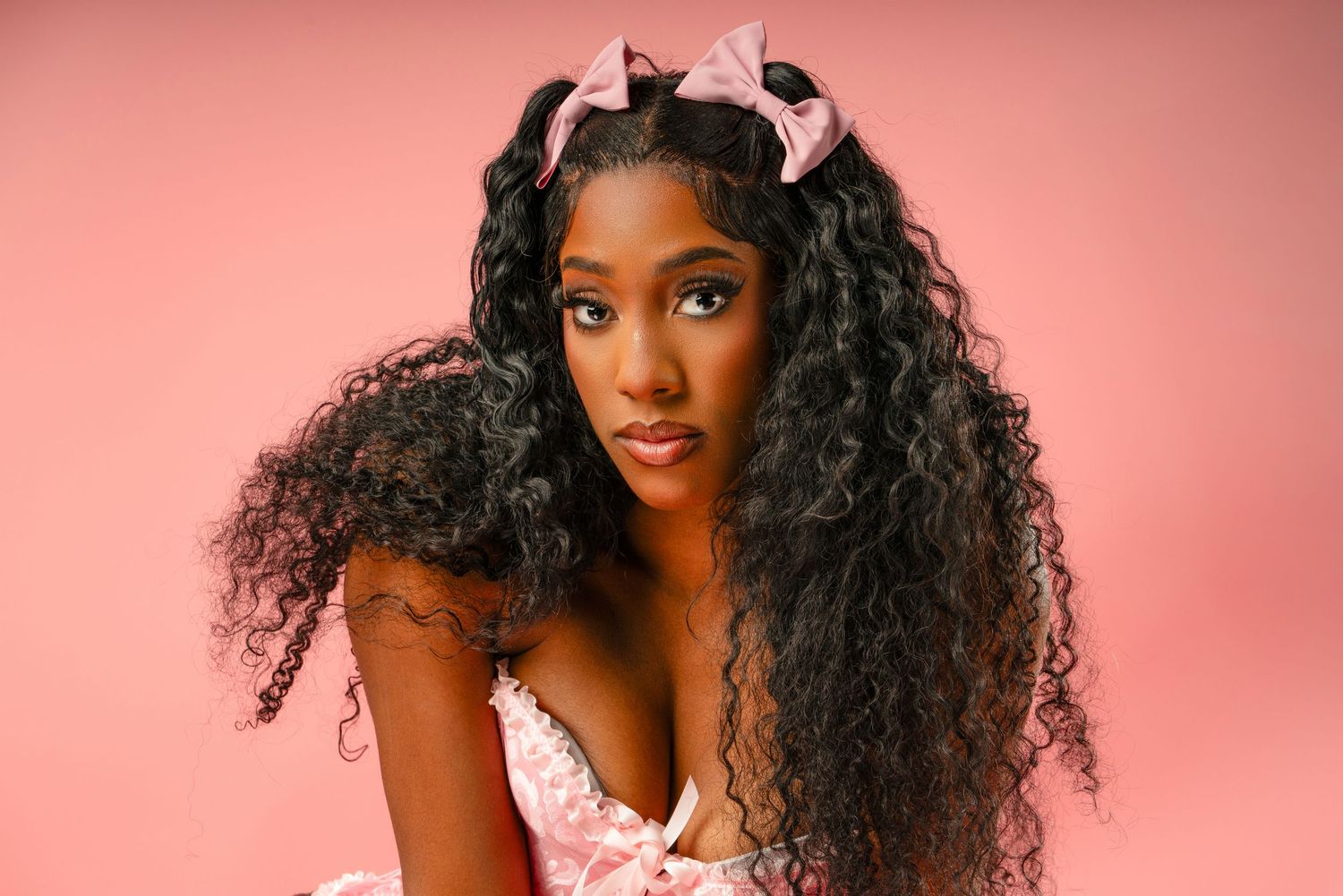 Closeup beauty shot with long curly hair and white bow accessories against pink background.