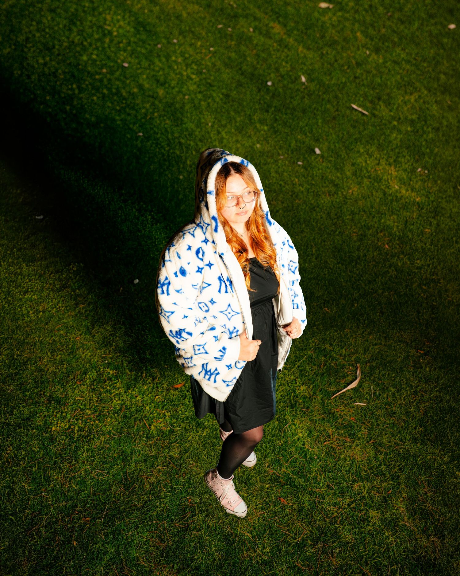 Young woman in Louis Vuitton hooded jacket and black dress standing on green grass lawn.