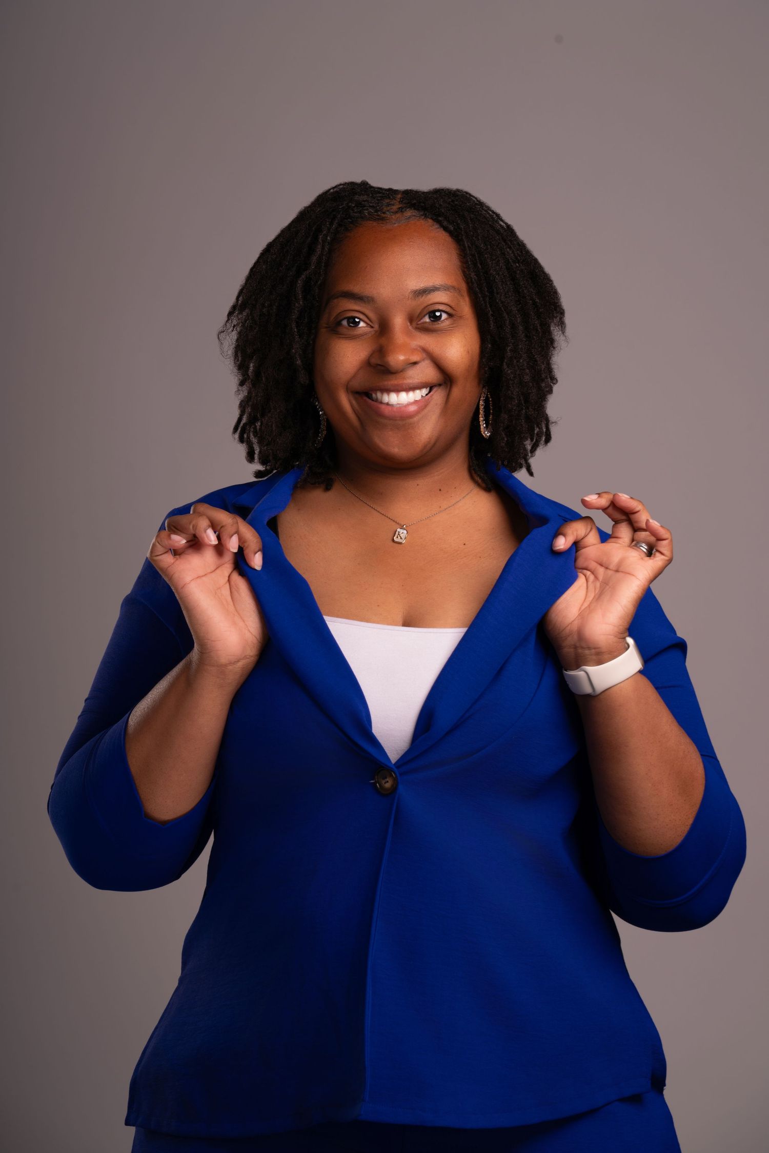 Joyful pose in a vibrant blue blazer with hands raised in an energetic gesture.