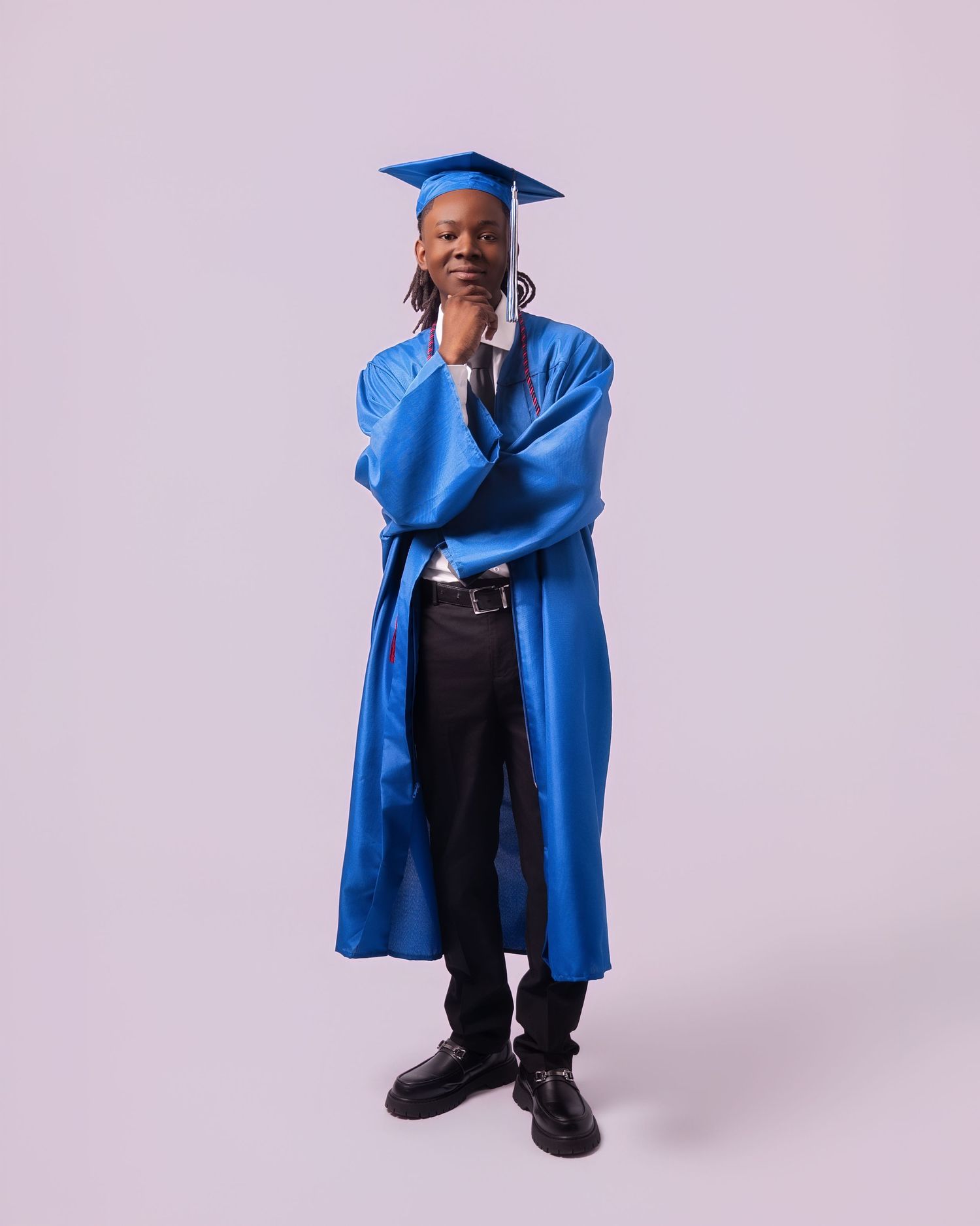 Person wearing a blue graduation cap and gown poses thoughtfully against a light gray background.