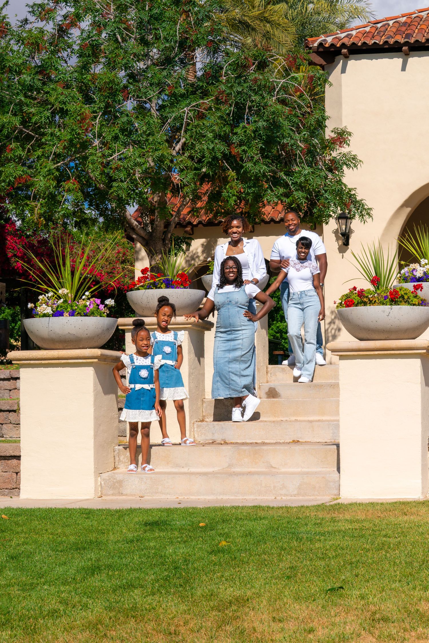 A group poses on Mediterranean-style stone steps with potted plants and arches in the background.