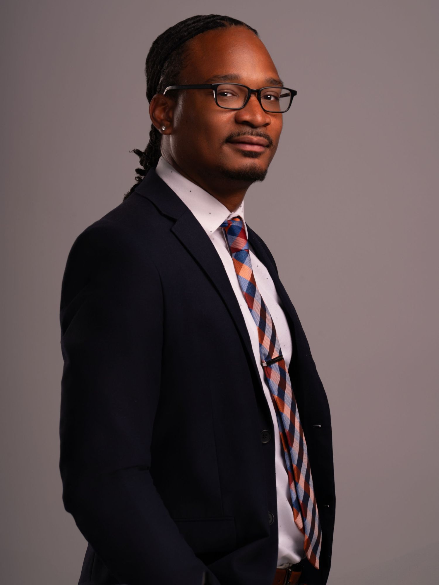 Side profile business portrait featuring navy suit, patterned tie and glasses.