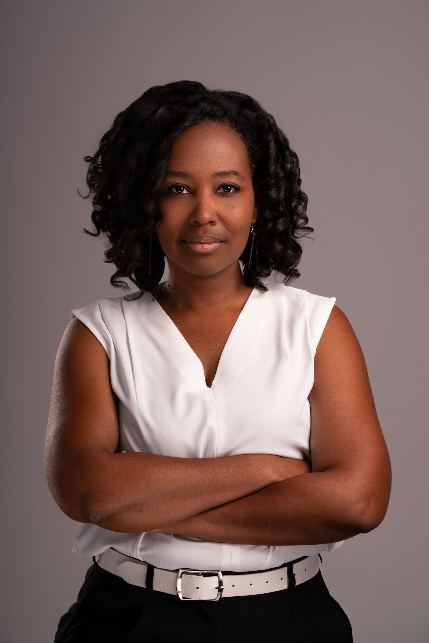 Business portrait in white sleeveless top with belt against studio background.