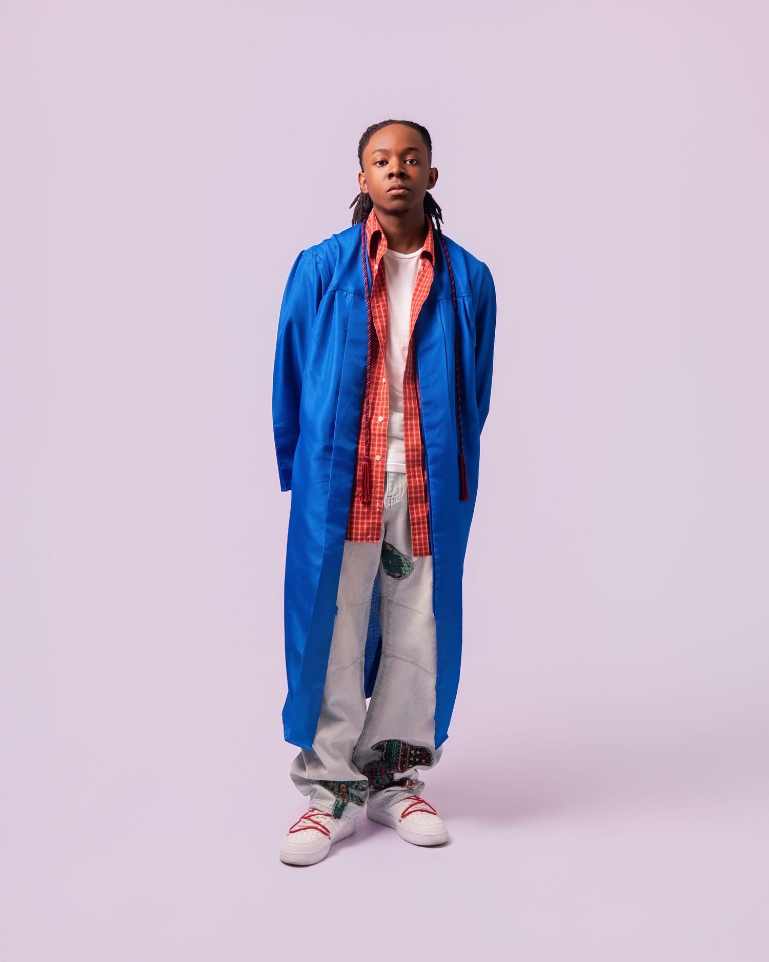 Young person wearing a blue longline coat over a red plaid shirt with grey jeans and white sneakers.
