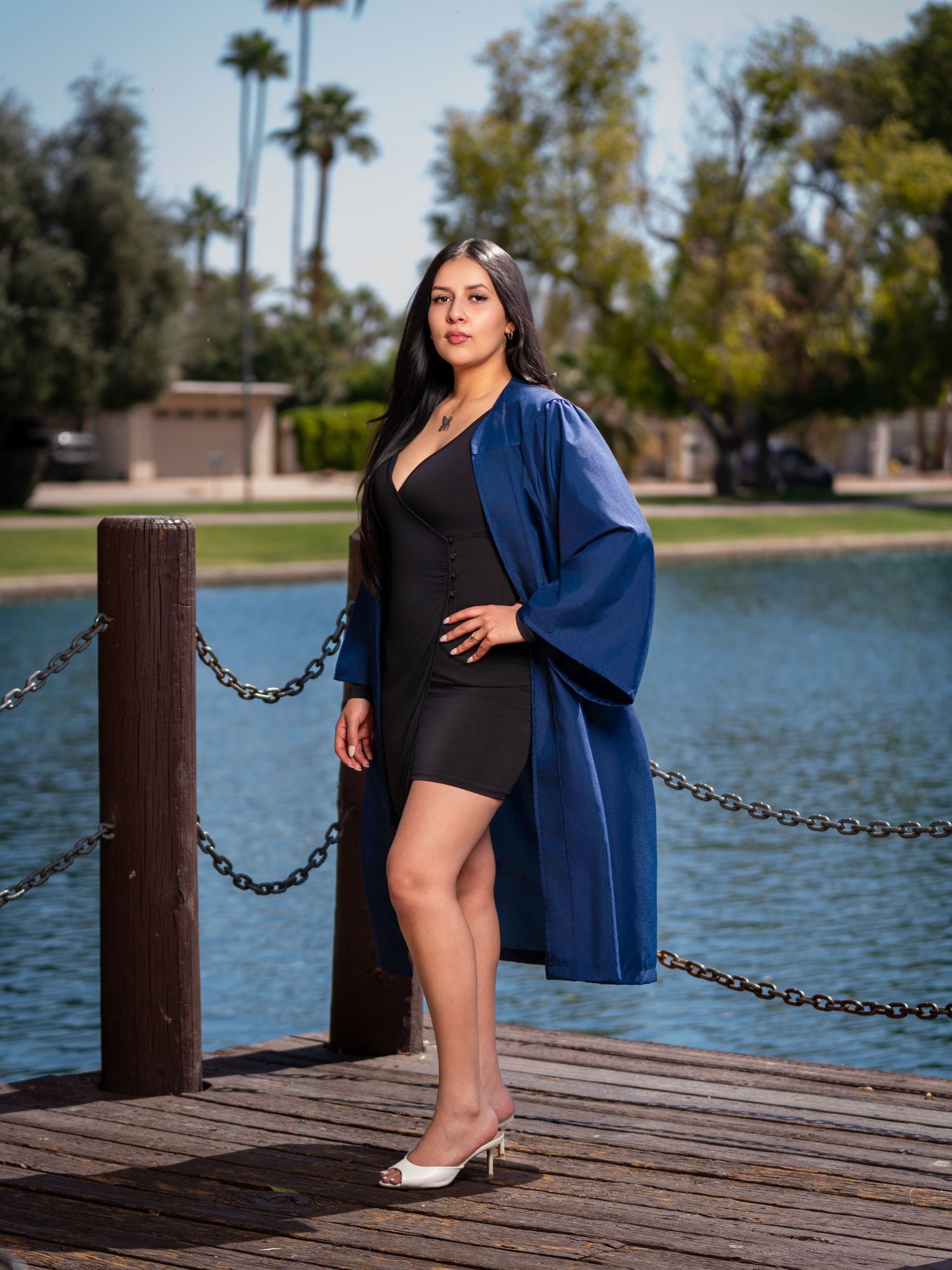 Stylish portrait session at a lakeside dock featuring a black dress and blue shawl against palm trees and water.