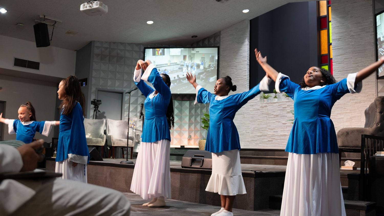 Performers in coordinated blue and white outfits stand together during a stage performance.