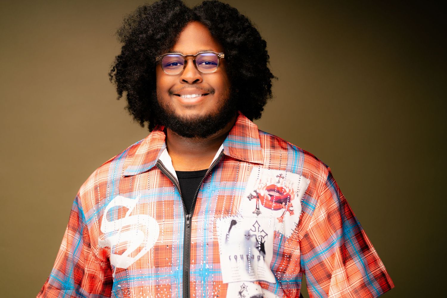 Casual portrait shot of person in plaid shirt and glasses against brown background.
