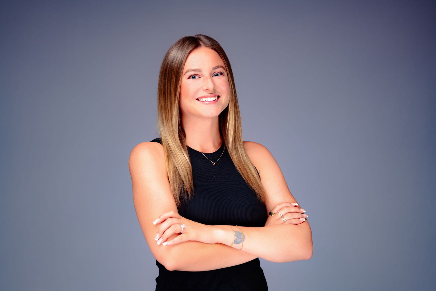 Professional headshot photo against dark background showing confident pose with crossed arms and black sleeveless top.