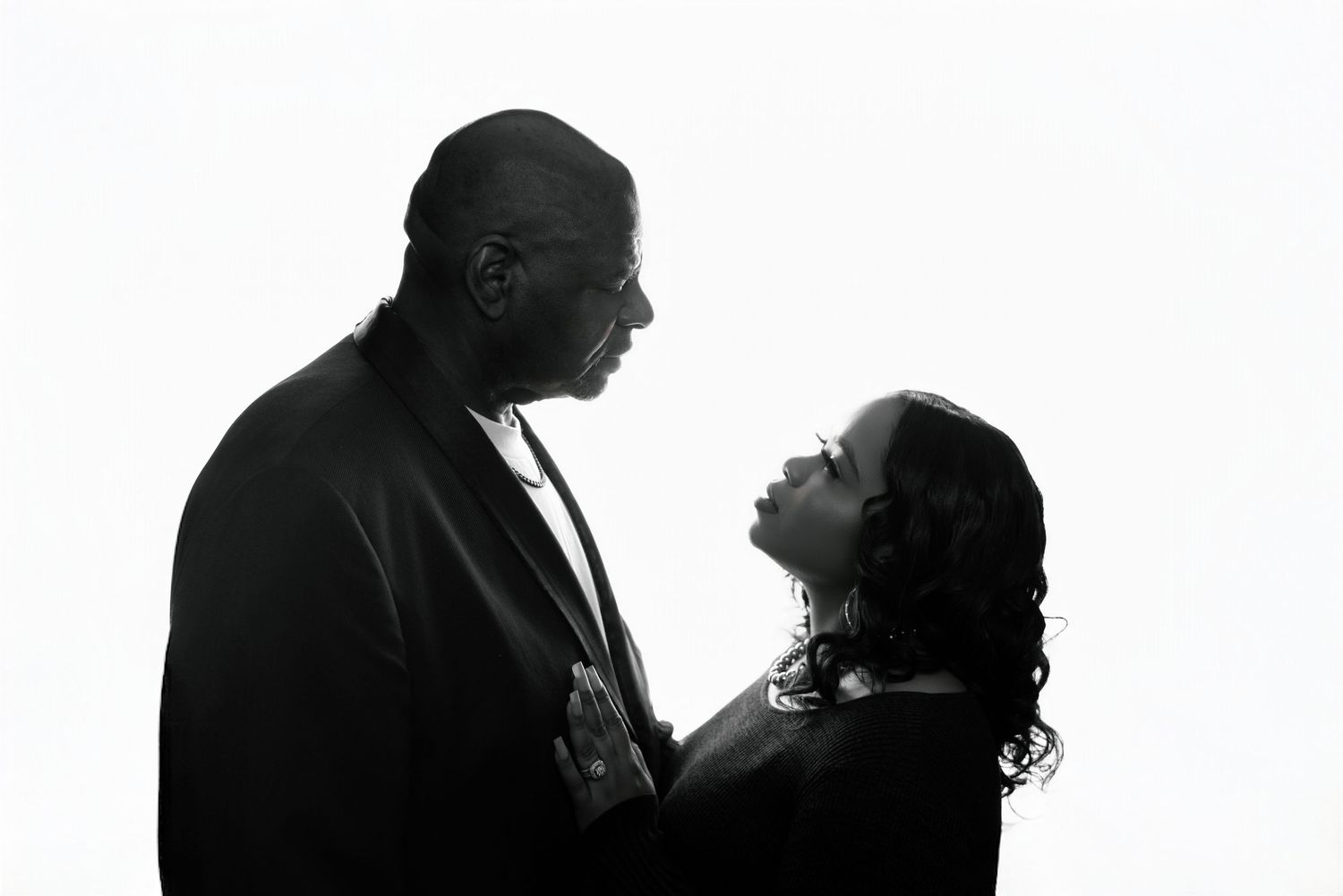 A silhouetted couple in profile against a white background share an intimate moment together.