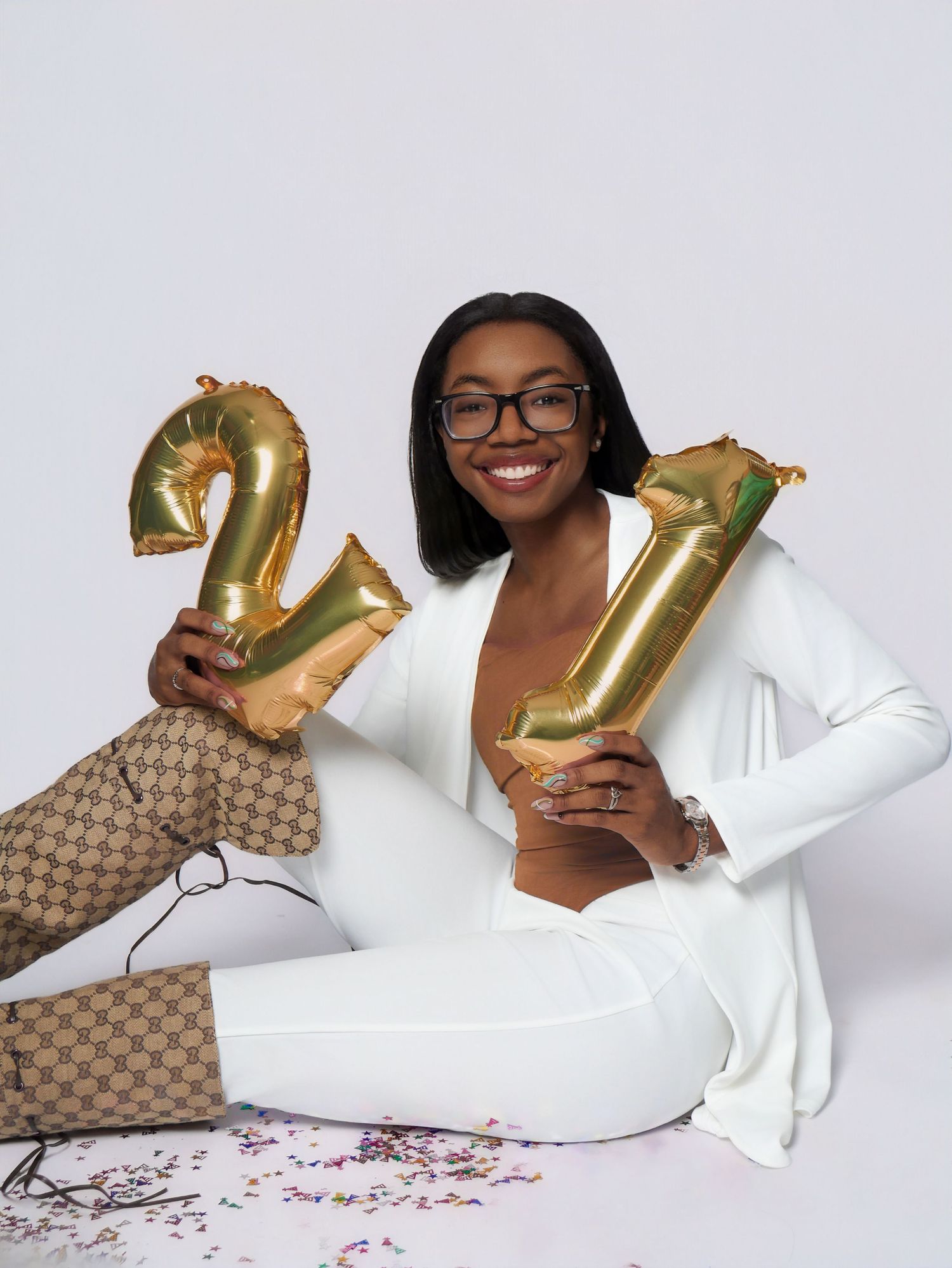 Person holds gold number 21 balloons while wearing white blazer in celebration photo.