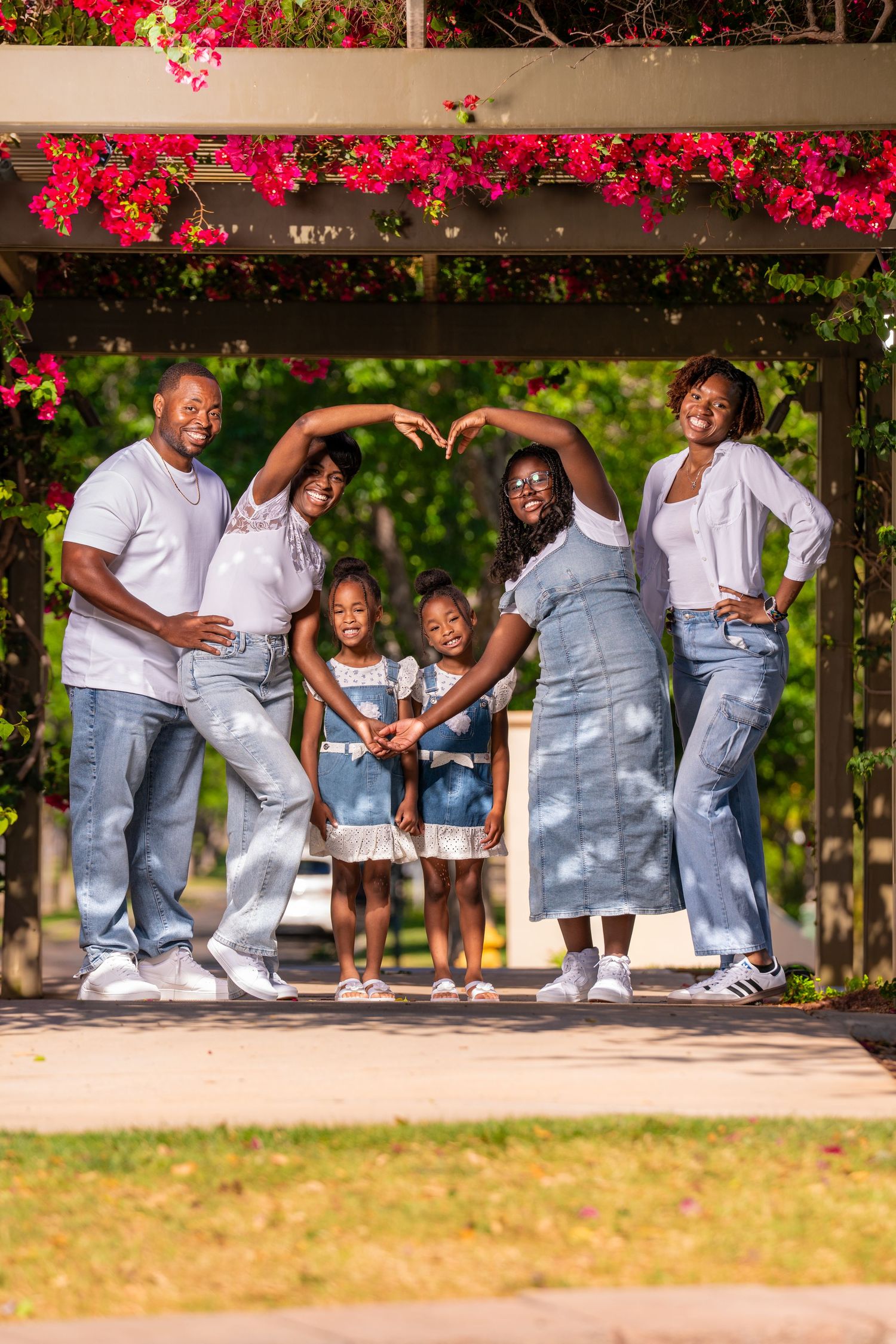 Family photo under pergola with bright red flowers, wearing coordinated white tops and denim.