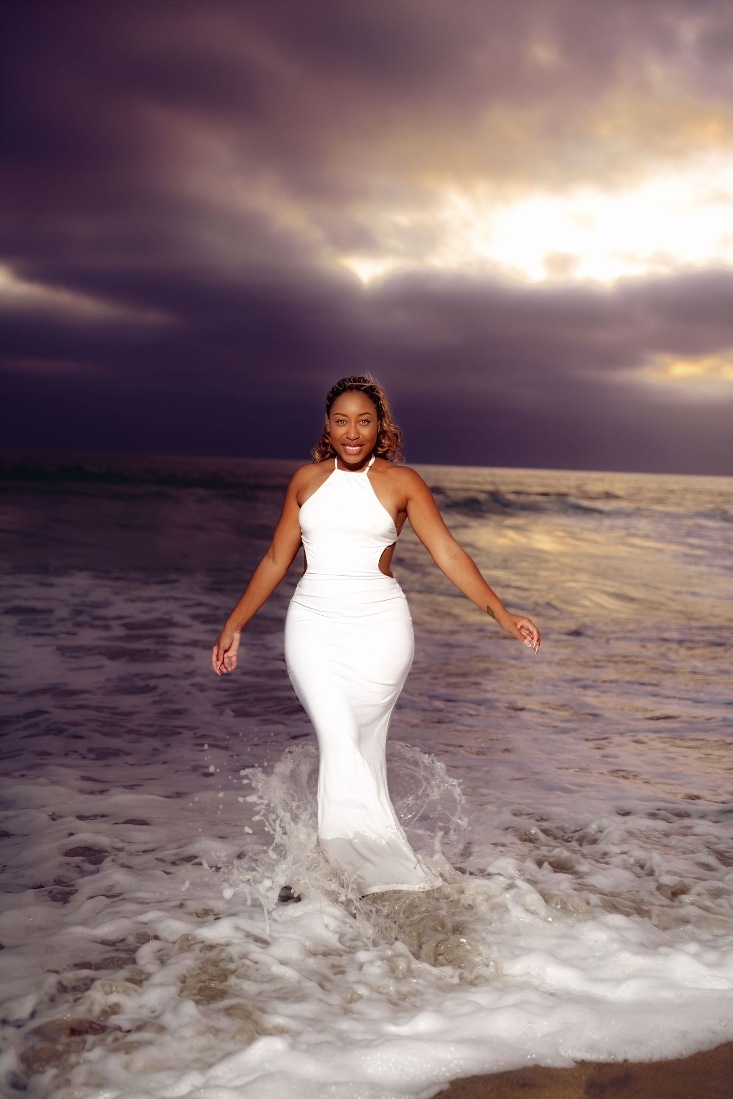 Dynamic beach photography session with splashing waves and dramatic sunset sky.