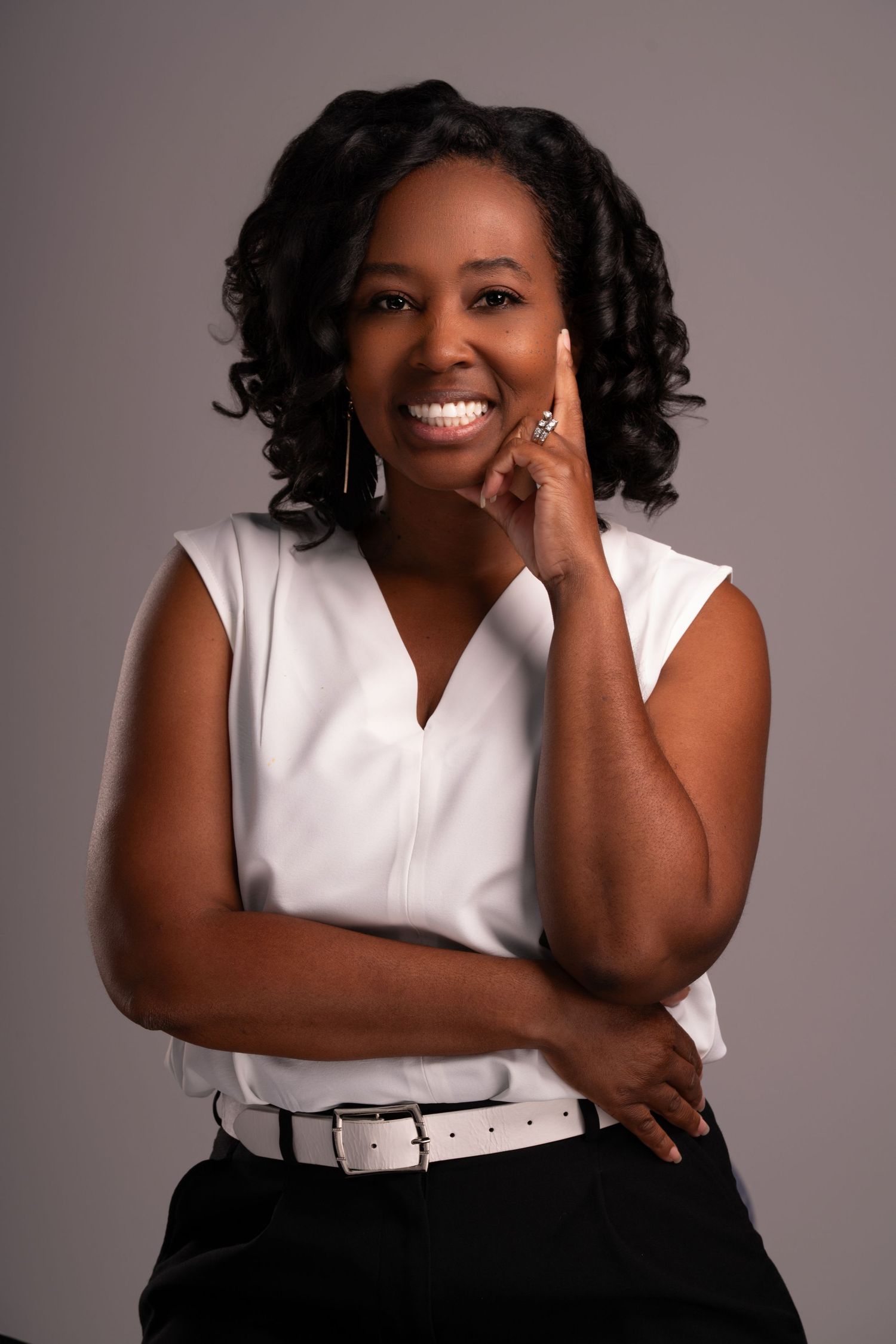 Professional portrait in white sleeveless top with silver accessories against gray background.
