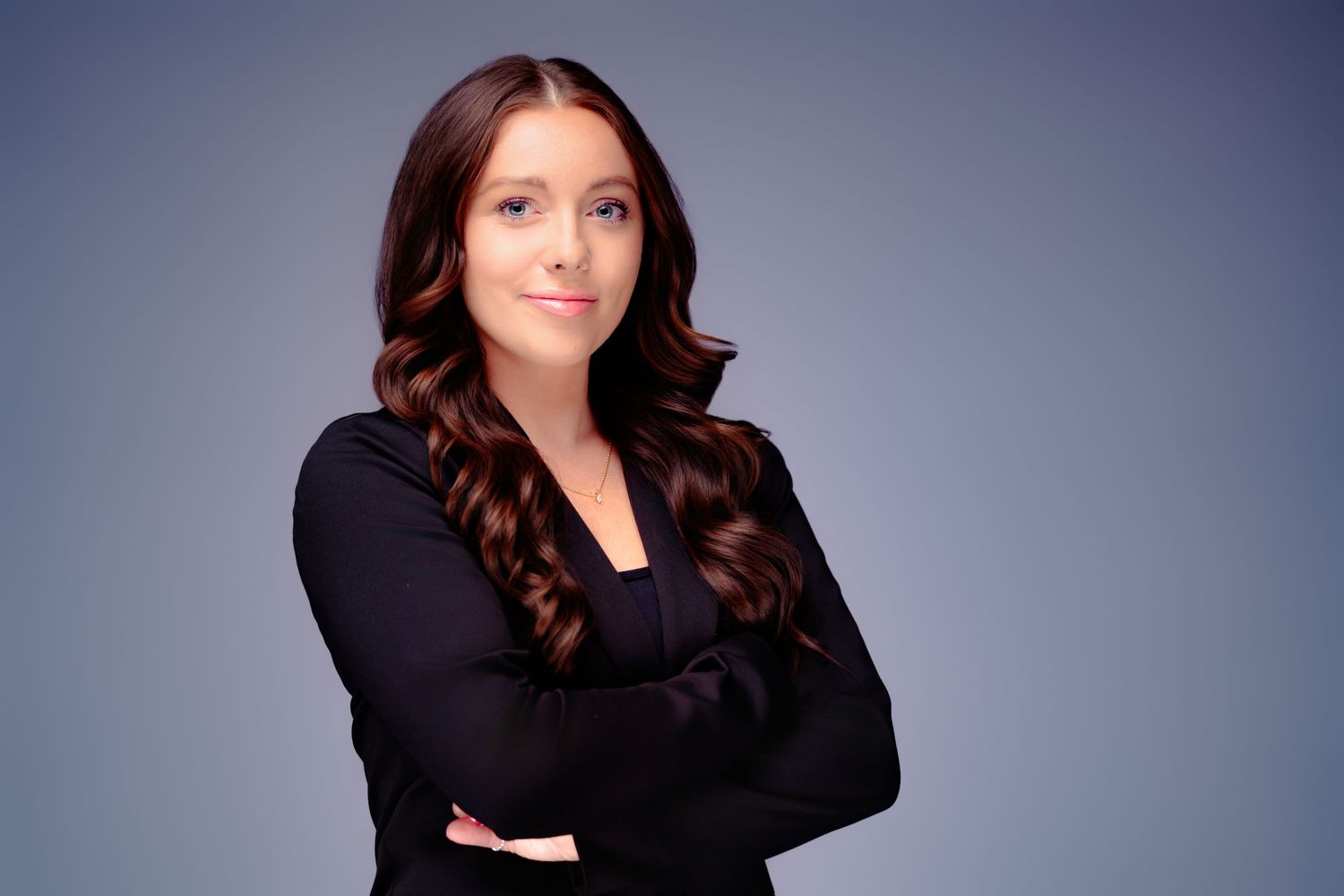 Professional headshot featuring a warm smile and wavy dark hair against a blue-gray backdrop.