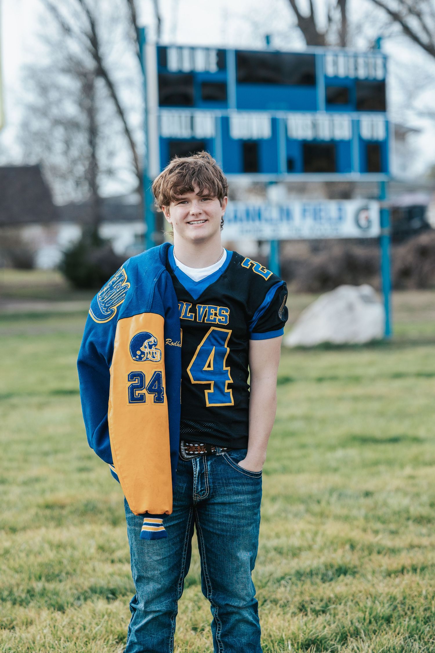High school athlete in blue and gold football jersey poses outdoors for sports portrait session.