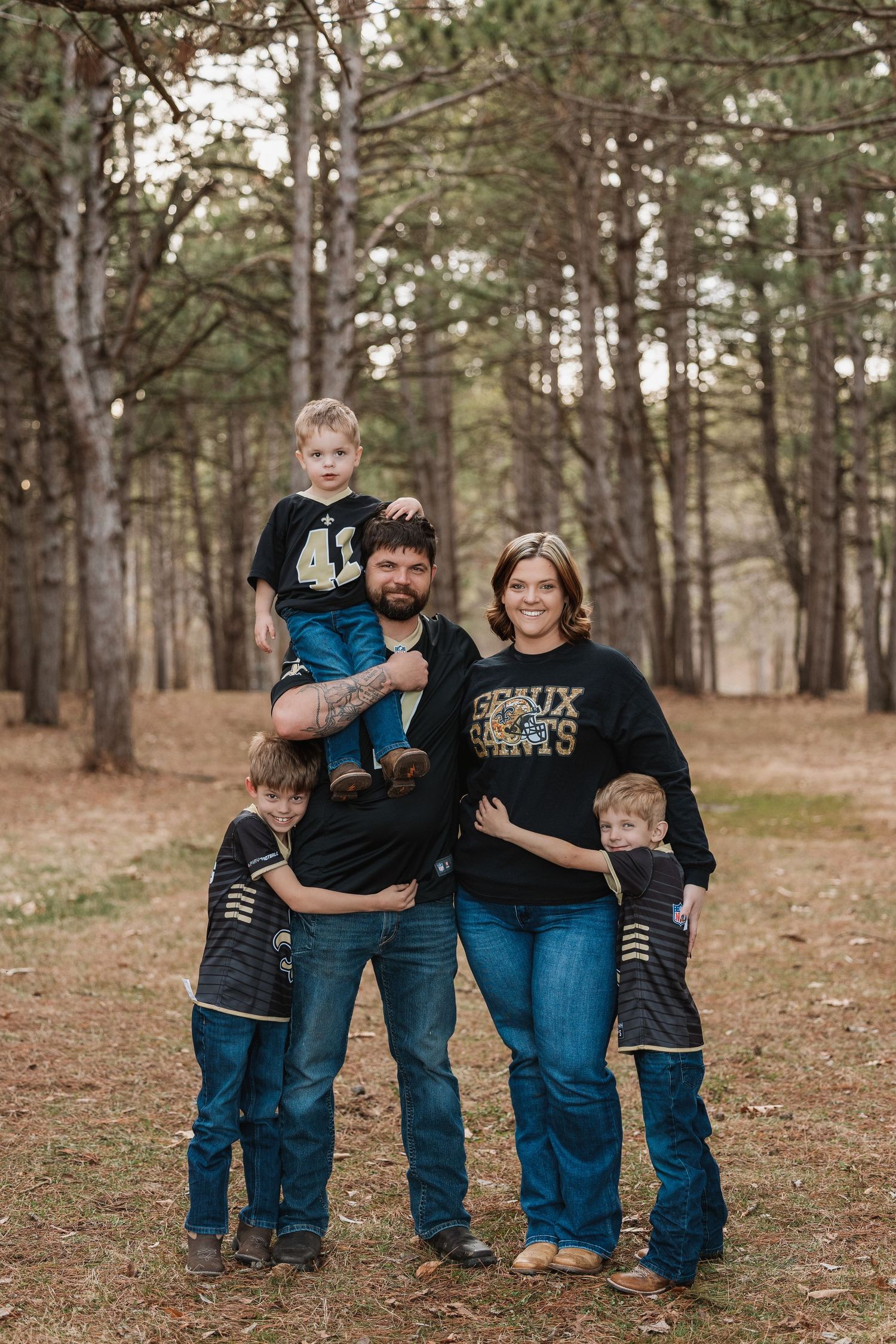 A family wearing coordinating casual outfits poses together in a pine forest during autumn.