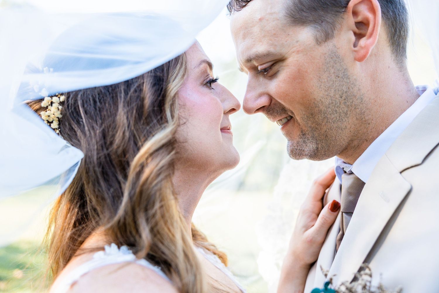 A romantic couple shares a tender kiss on a sunny beach with soft natural lighting and ocean waves in the background.