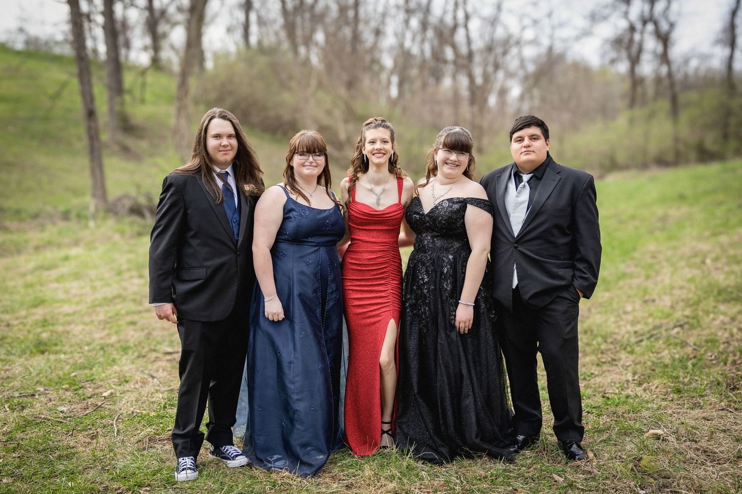 Group of people in formal attire standing together outdoors in a natural wooded setting during springtime.