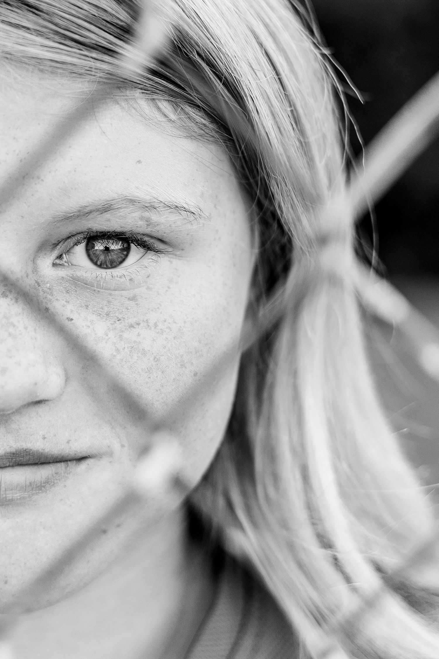 Artistic black and white close-up portrait showing half of face with windswept hair.