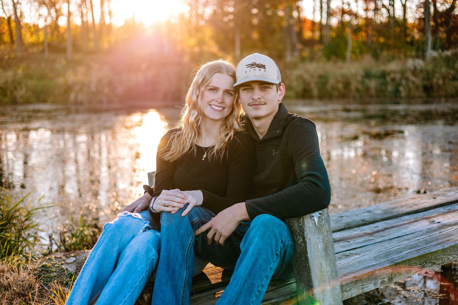 Romantic sunset engagement session at wooden dock by tranquil lake.