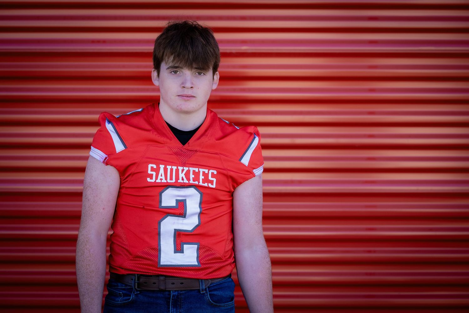 Senior portrait series against red metal garage door background in sports uniform.