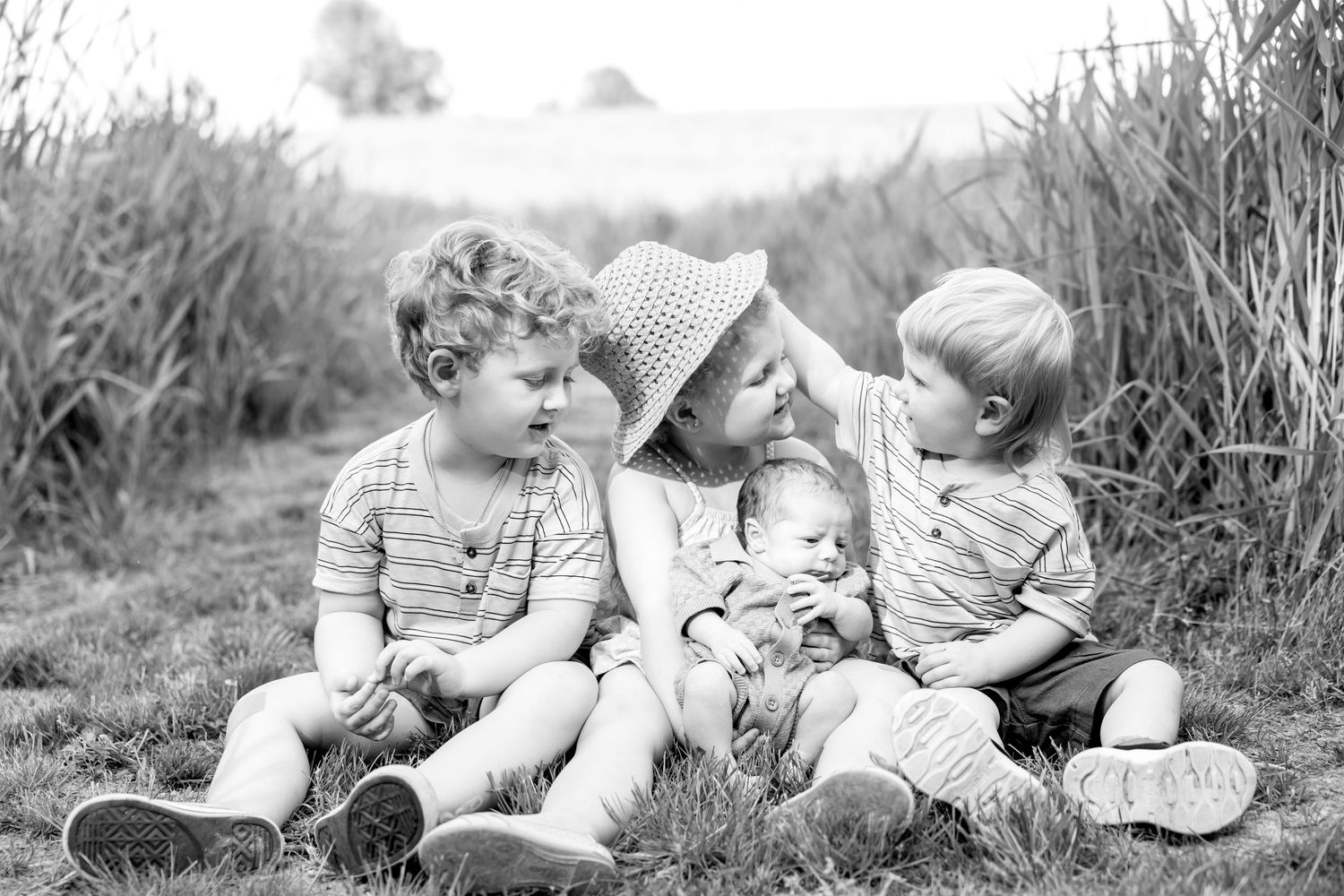 Sweet outdoor portrait session of small children sitting together in a rustic field setting.