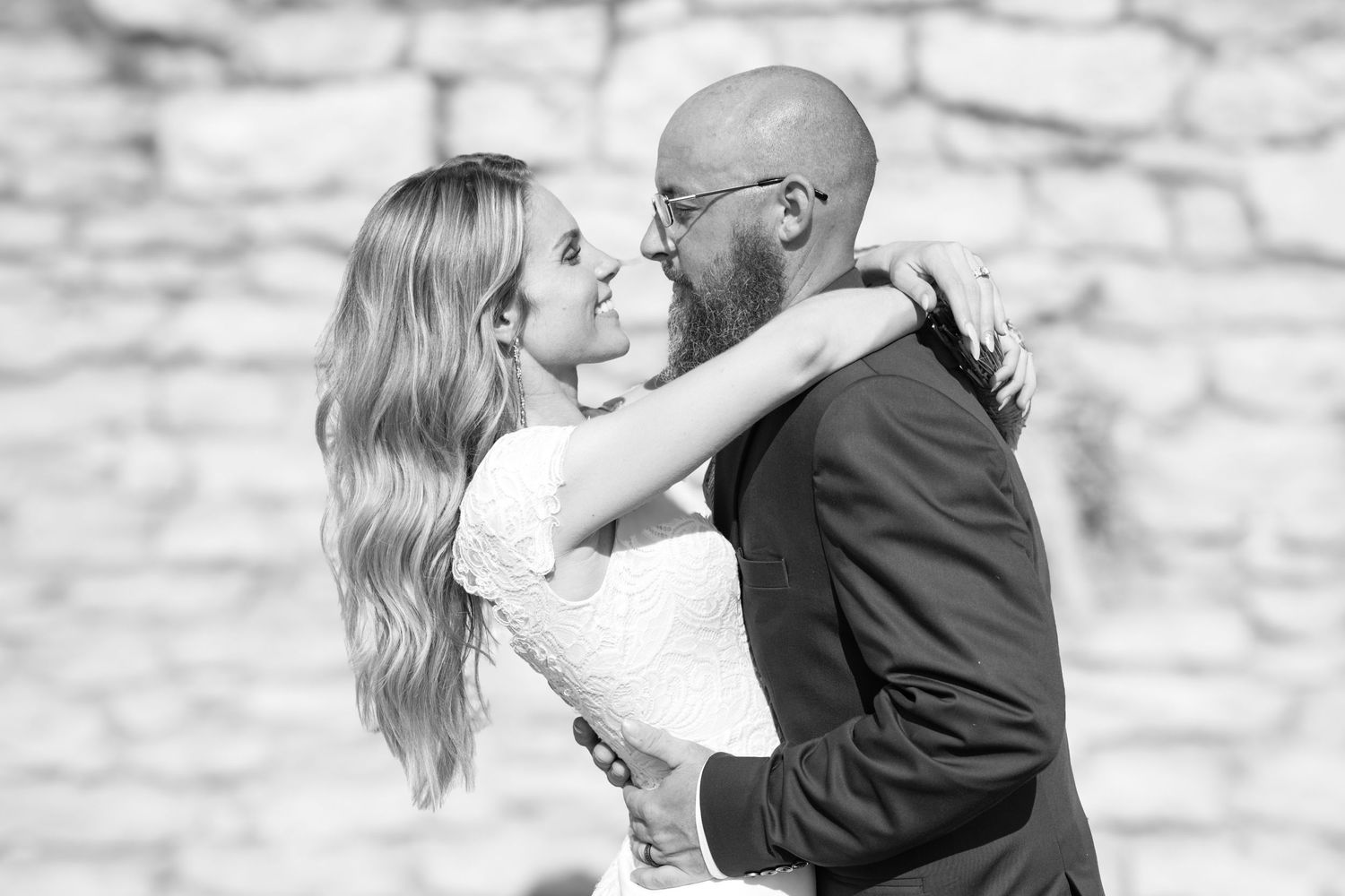 Black and white romantic wedding photos showing tender moments between a couple against a stone wall background.