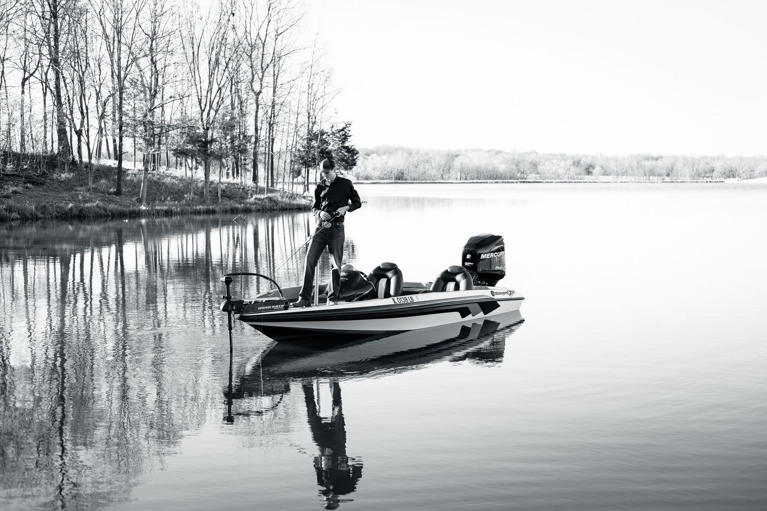 Silhouette of angler fishing from boat on calm lake during early morning.