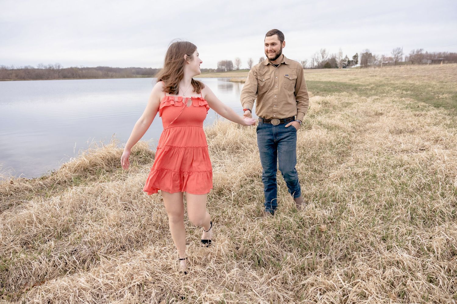 Romantic couple poses in a grassy field during sunset engagement photo session.