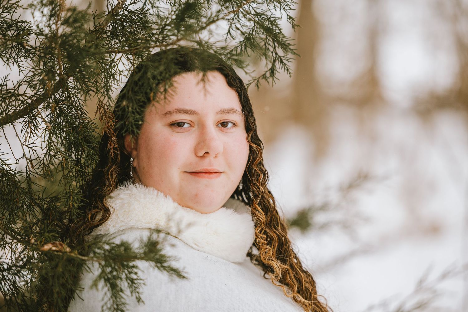 A snowy winter portrait session in the woods with evergreen branches framing the ethereal scene.