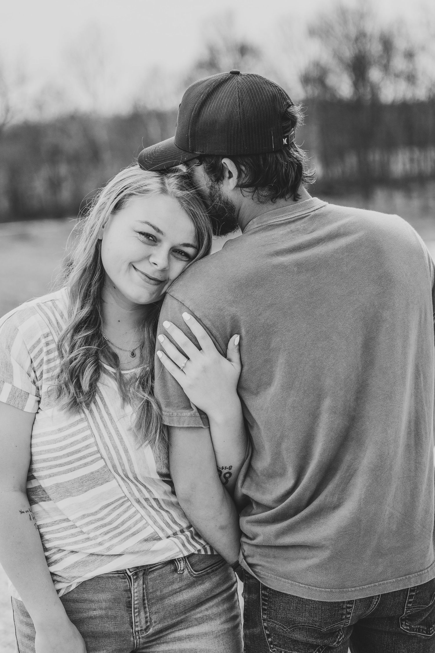 Black and white photo of a young couple sharing a tender moment outdoors, woman smiling softly.