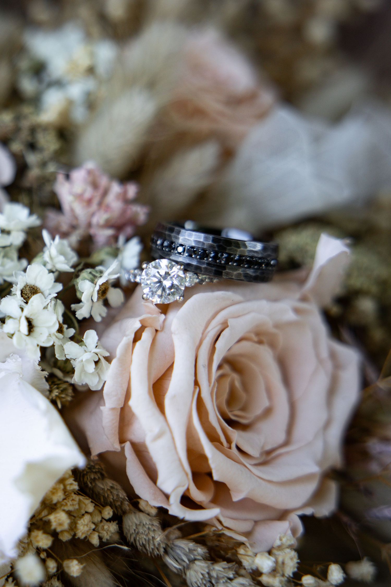 Wedding rings nestled among delicate pink roses and baby's breath flowers on a textured surface.