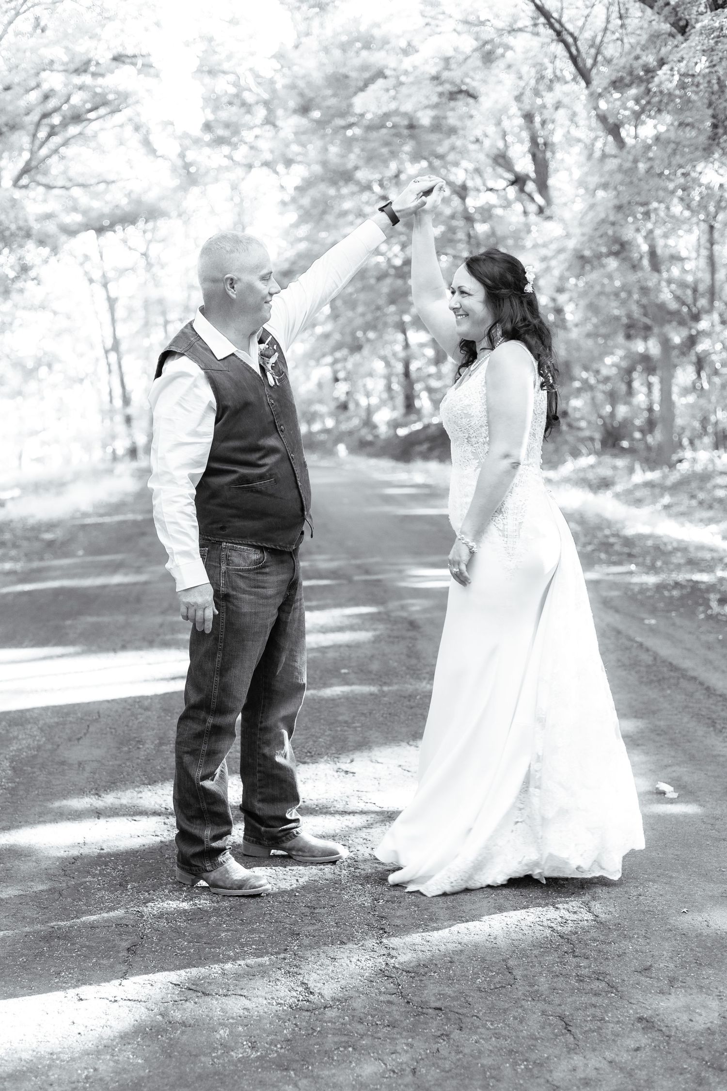 Black and white portrait of couple celebrating joyful moment on tree-lined path.